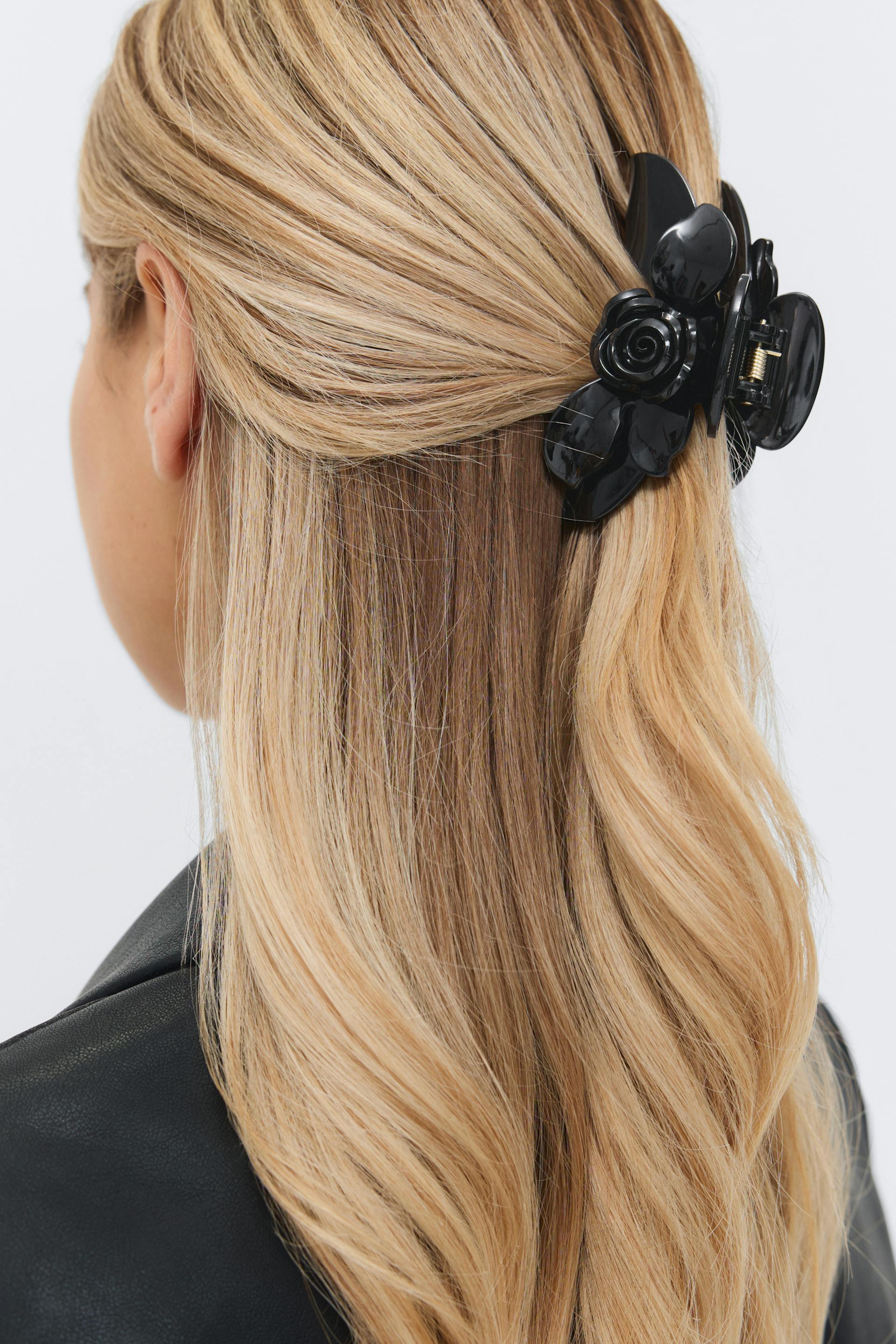 Black floral-shaped claw hair clip securing half-up blonde hair, with a black leather jacket visible at the shoulder.