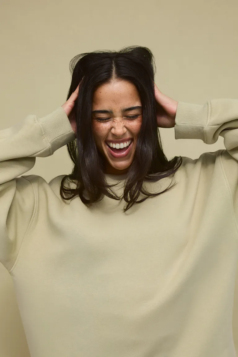 Kvinde iført en oversized lys beige sweatshirt med rund hals og ribbede manchetter.