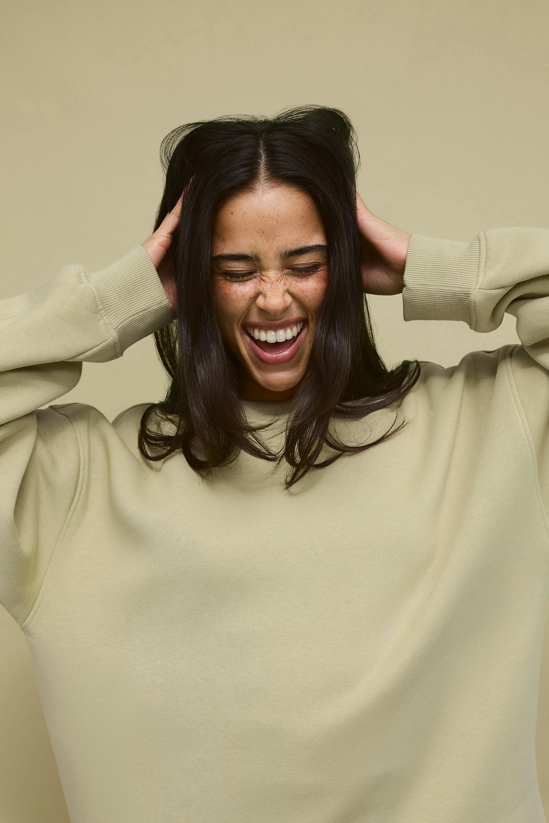 Woman wearing an oversized light-beige crewneck sweatshirt with ribbed cuffs.