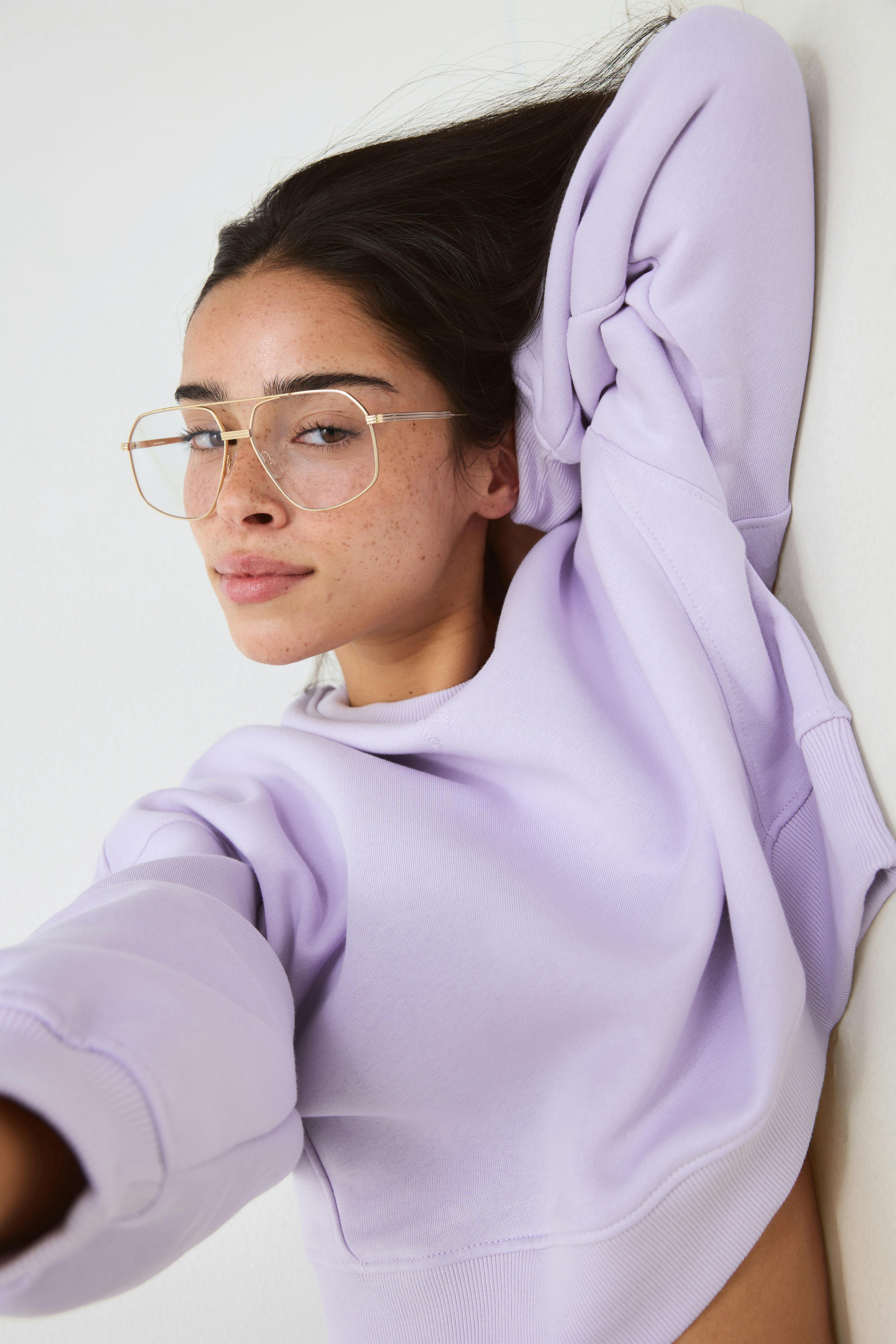 Lett lavendelfarget sweatshirt med rund hals kombinert med store aviatorbriller med gullramme.