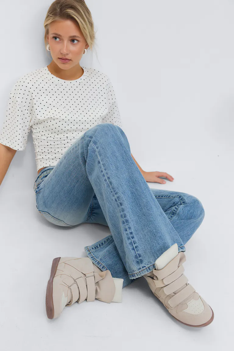 Hvit kortermet, figursydd topp med svarte mikroprikker, lyse, høytaljede jeans med vidde, beige, høye sneakers med flere borrelåsstropper og kremfarget tunge.