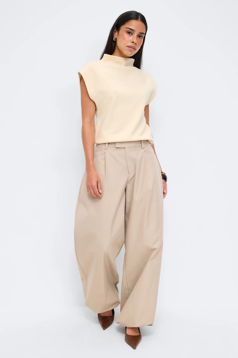 Cream mock-neck sleeveless top paired with high-waist beige wide-leg pleated trousers and brown pointed-toe heels.
