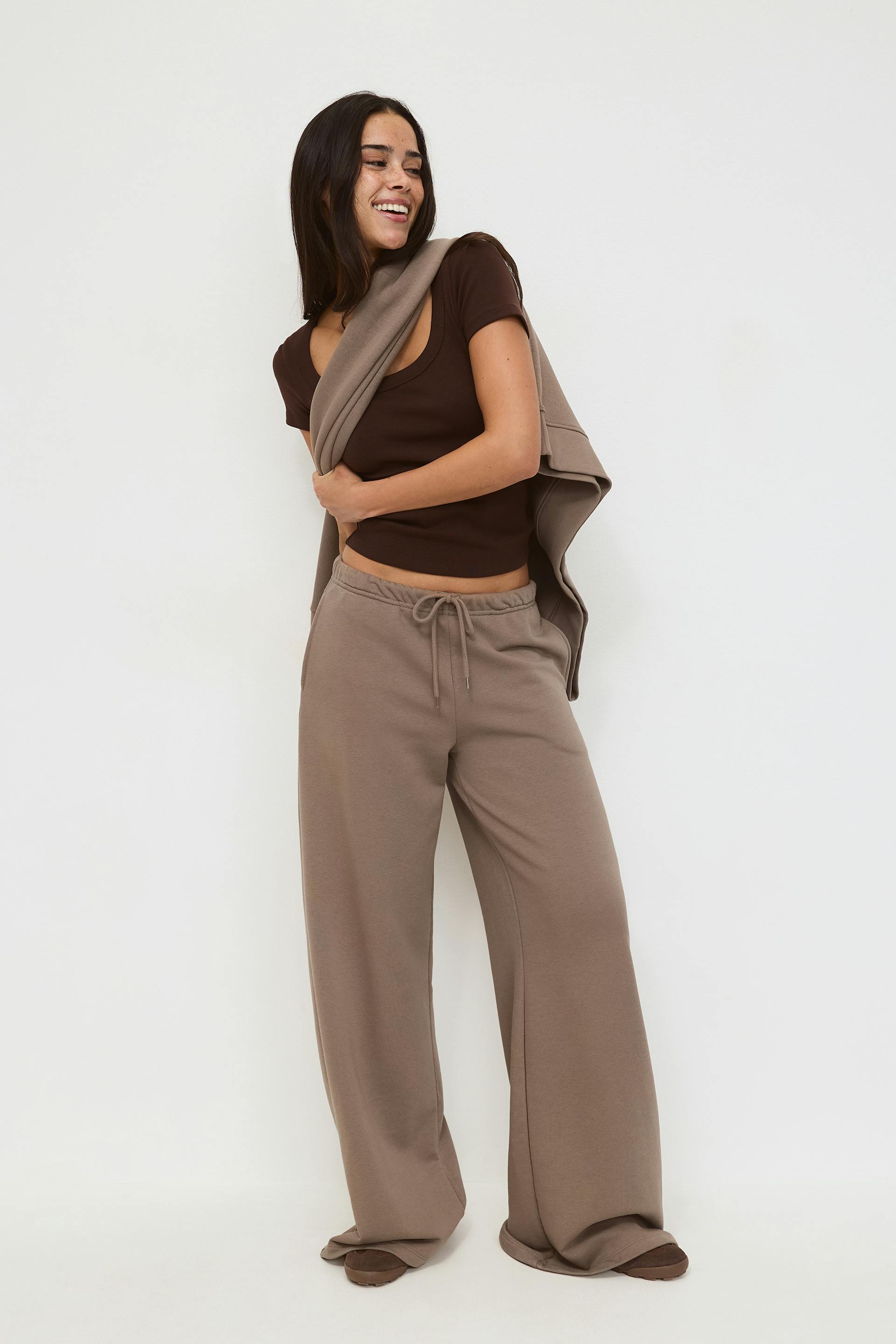 Taupeen värinen kengurutaskuinen huppari, johon on yhdistetty yhteensopivat leveälahkeiset vetoketjulliset collegehousut ja mustat neliskanttiset kengät.