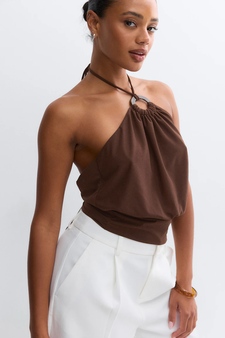Braunes Neckholder-Top mit Metallring-Detail und gerafftem Ausschnitt, das mit einem taillierten Saum abschließt, gepaart mit einer weißen, hoch taillierten Hose.