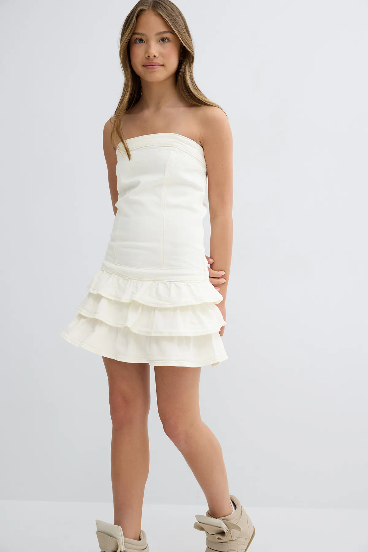 Mini robe bustier blanc cassé avec un corsage ajusté et une jupe à volants à trois niveaux, associée à des baskets montantes beiges.