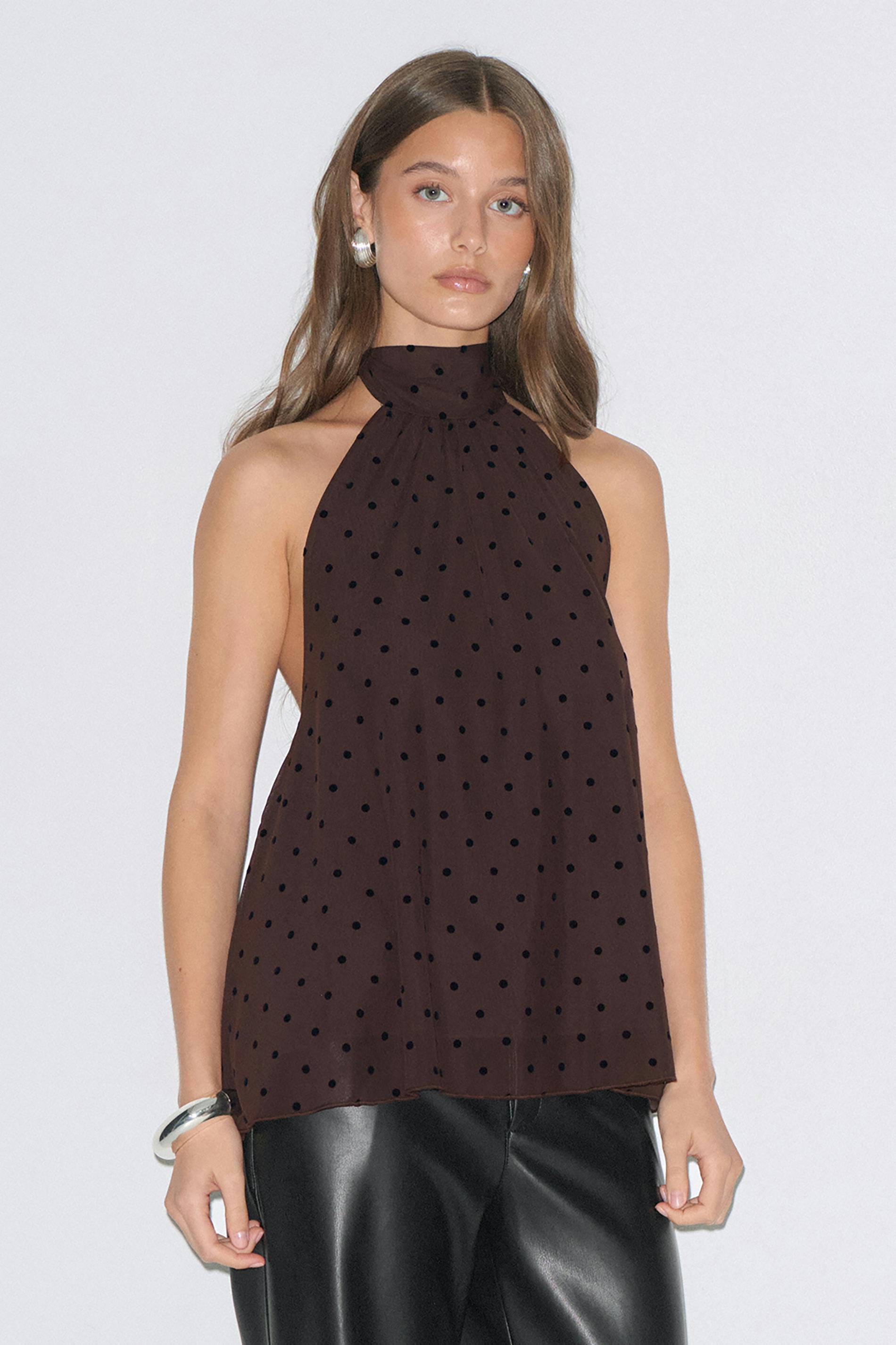 Hihaton korkeakaulainen ruskea pilkkupusero, johon on yhdistetty mustat nahkahousut, hopeiset korvakorut ja hopeinen rannerengas.