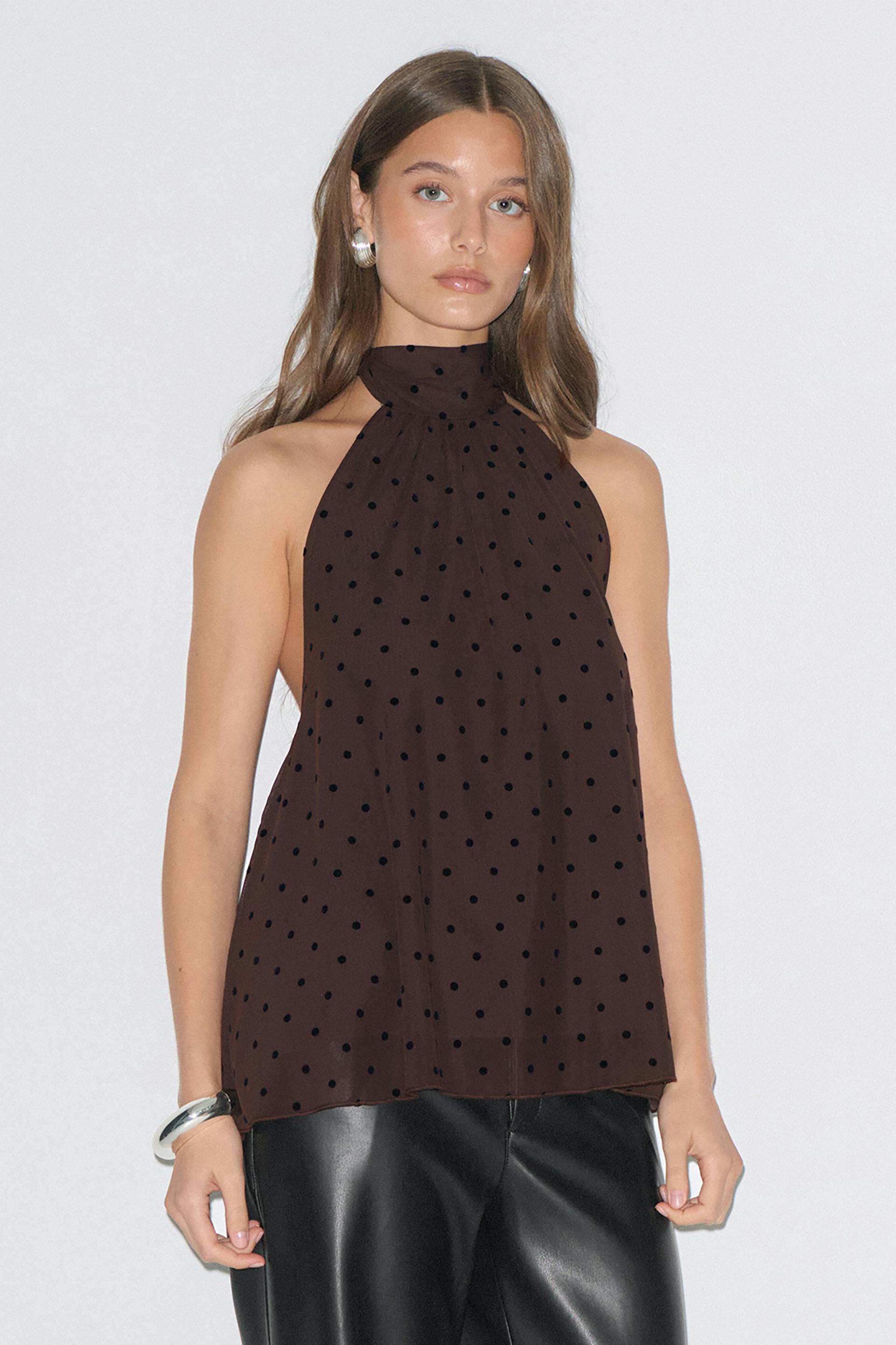 Hihaton korkeakaulainen ruskea pilkkupusero, johon on yhdistetty mustat nahkahousut, hopeiset korvakorut ja hopeinen rannerengas.