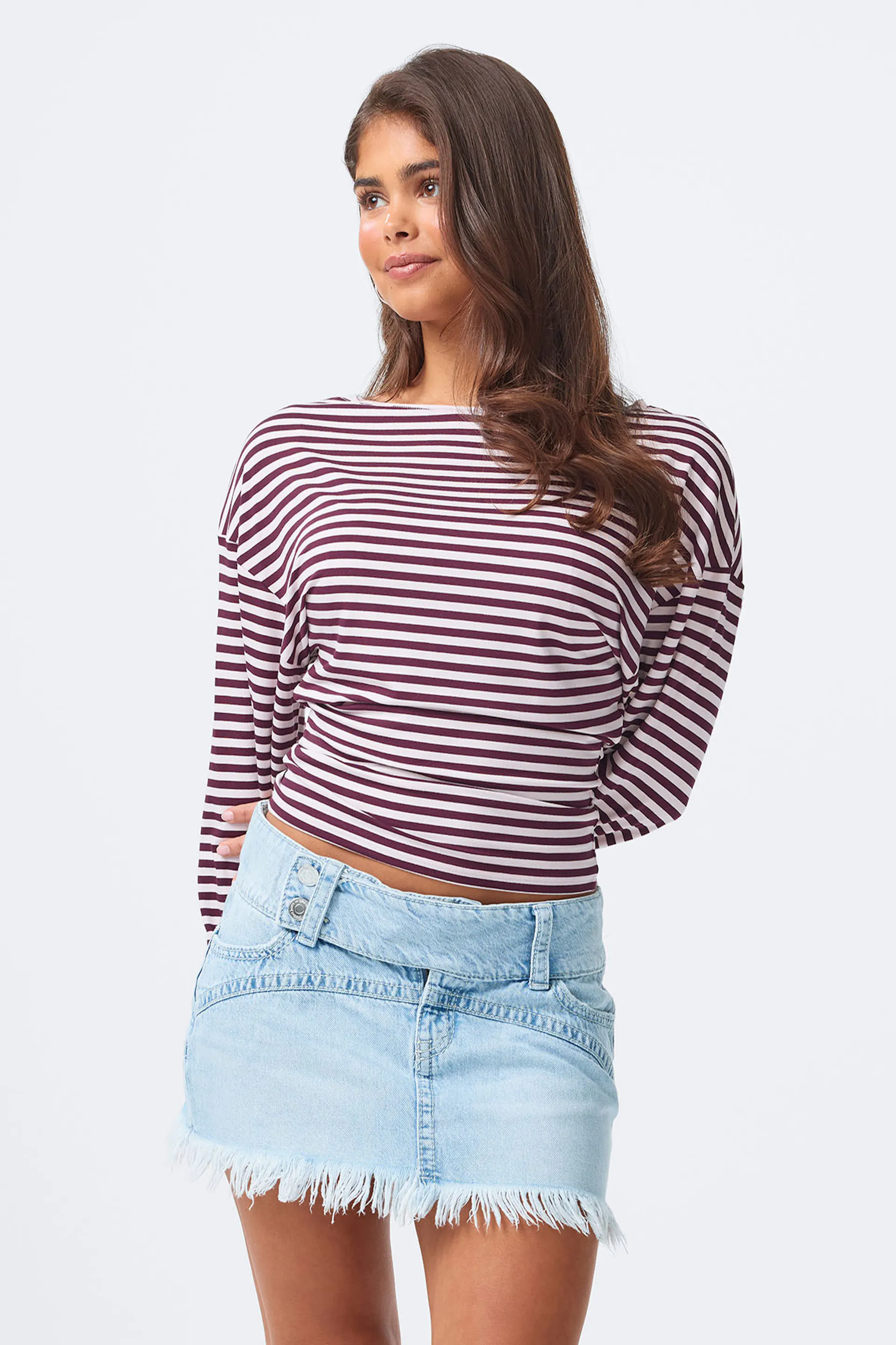 Rot-weißes, horizontal gestreiftes, langärmeliges Oberteil mit Rundhalsausschnitt, kombiniert mit einem hellen Jeansminirock mit ausgefranstem Saum und doppeltem Bund mit Knopf.