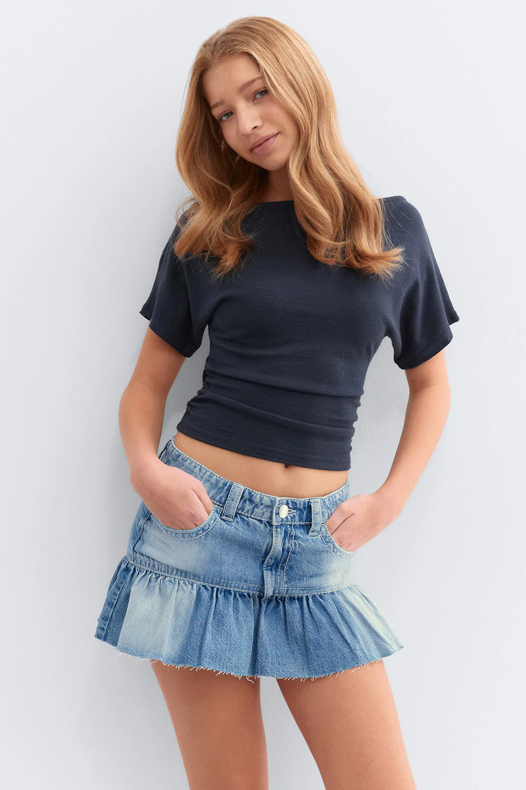 Navy getailleerde top met korte mouwen in combinatie met een lichtgekleurde denim minirok met zakken aan de voorkant, geknoopte tailleband en een gerafelde zoom met ruches.