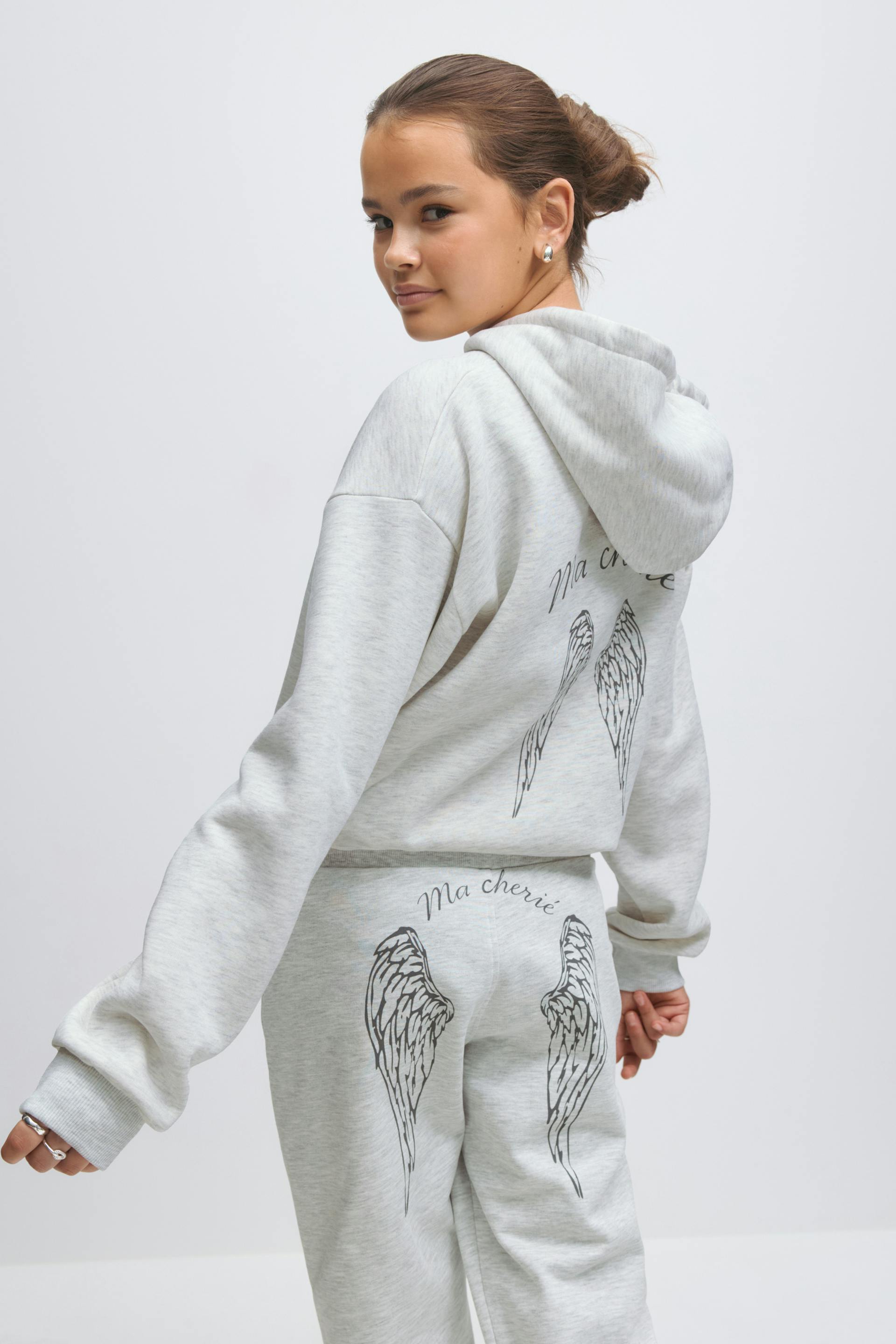 Light heather-gray hooded sweatshirt and matching sweatpants with black angel-wing prints and "Ma chérie" script on the back.