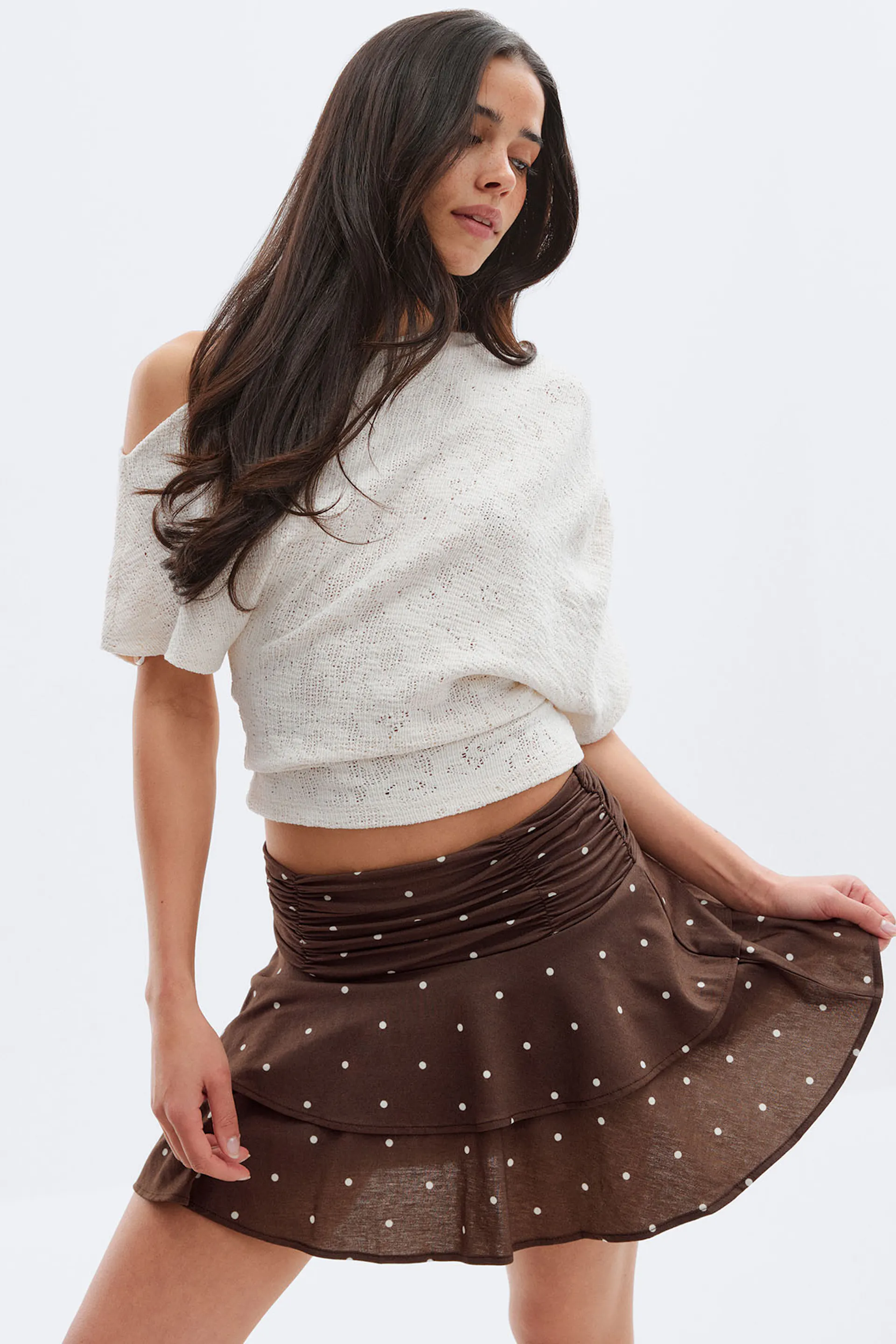 Kermanvärinen, olkapäätön, lyhythihainen neuletoppi yhdistettynä ruskeaan pilkulliseen monikerroksiseen minihameeseen, jossa on röyhelöinen vyötärönauha.