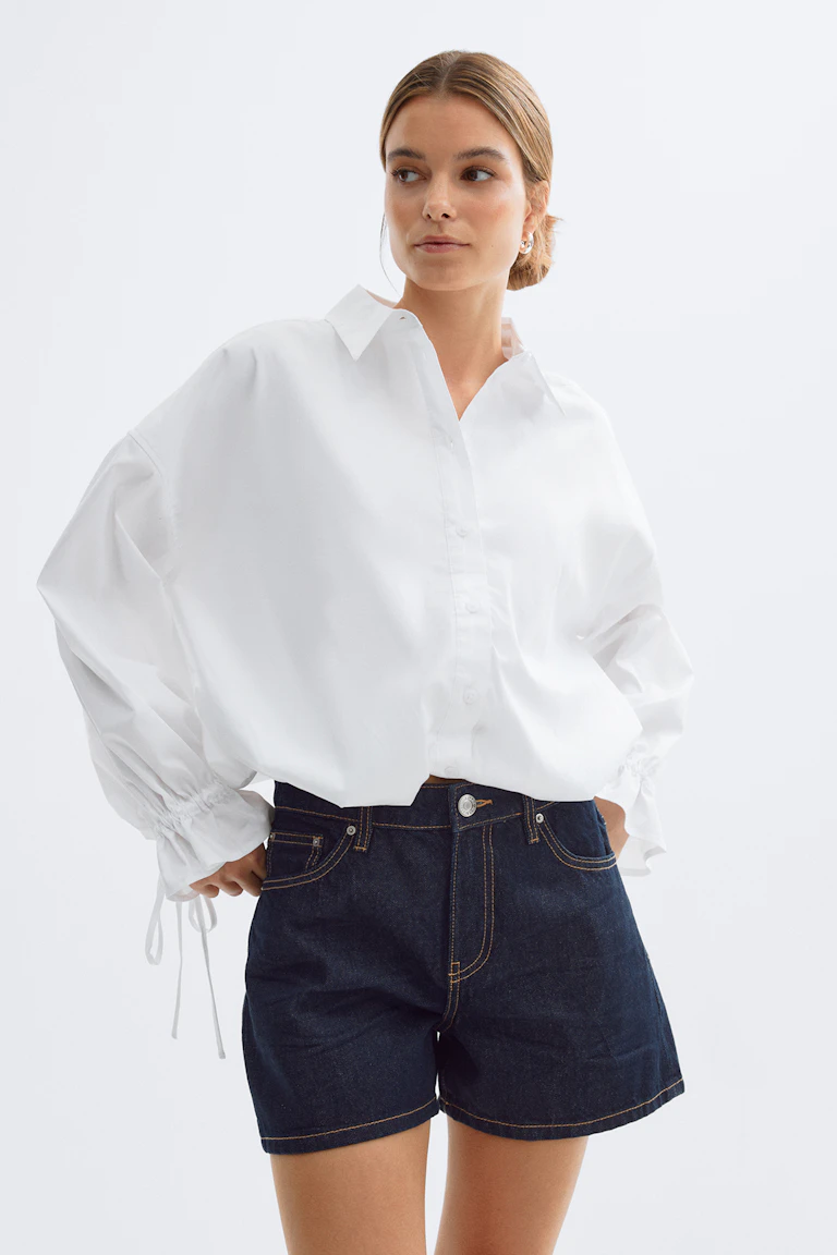 Oversized hvid button-down-skjorte med krave og lange, rynkede manchetter med snøre kombineret med mørke indigo denimshorts med kontrastsyninger.
