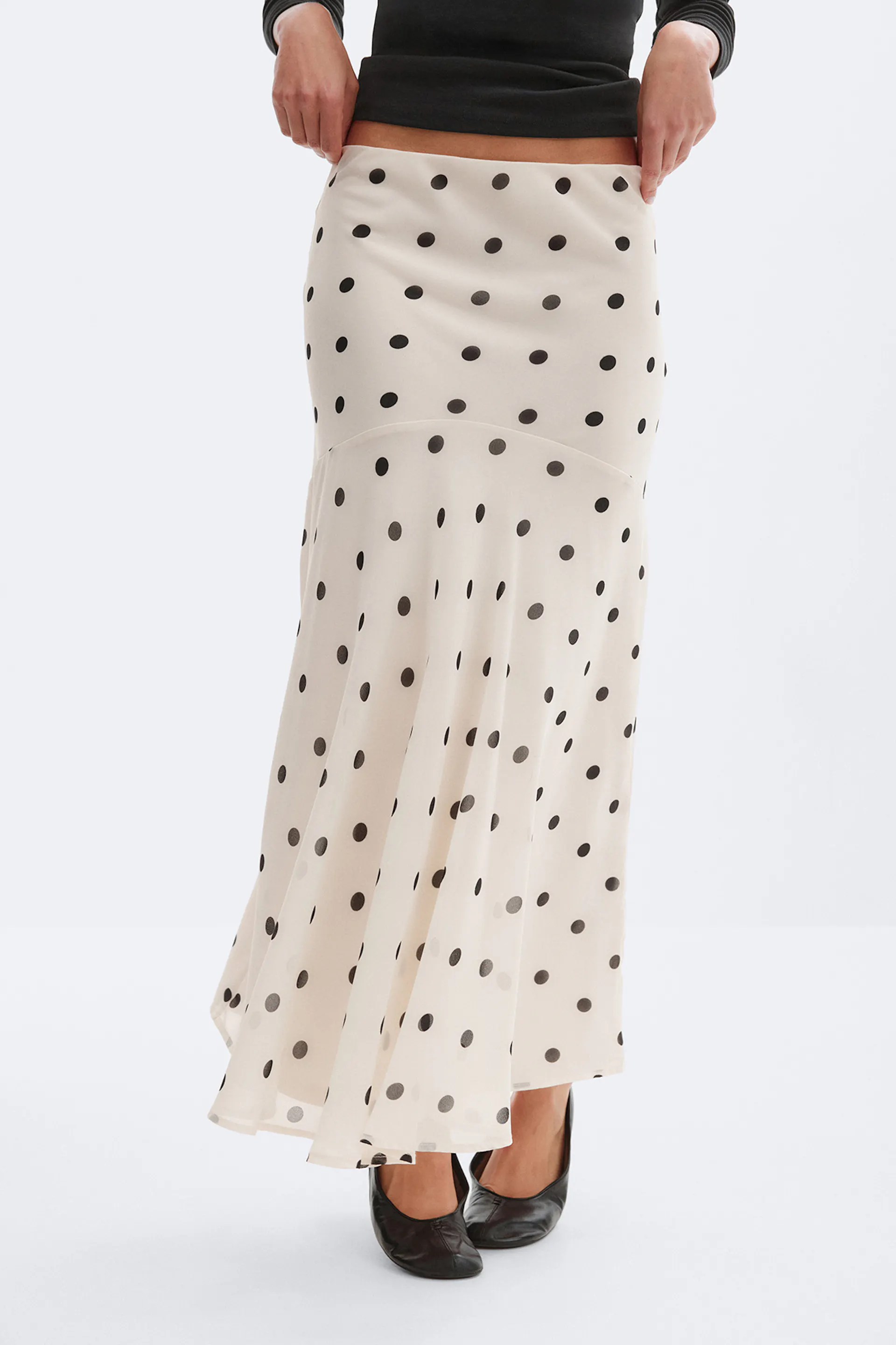 Kremfarget maxiskjørt med svarte prikker, figursydd over hoftene og utsvunget panelfåll, stylet med en svart, kortermet langermet topp og svarte skinnpumps.