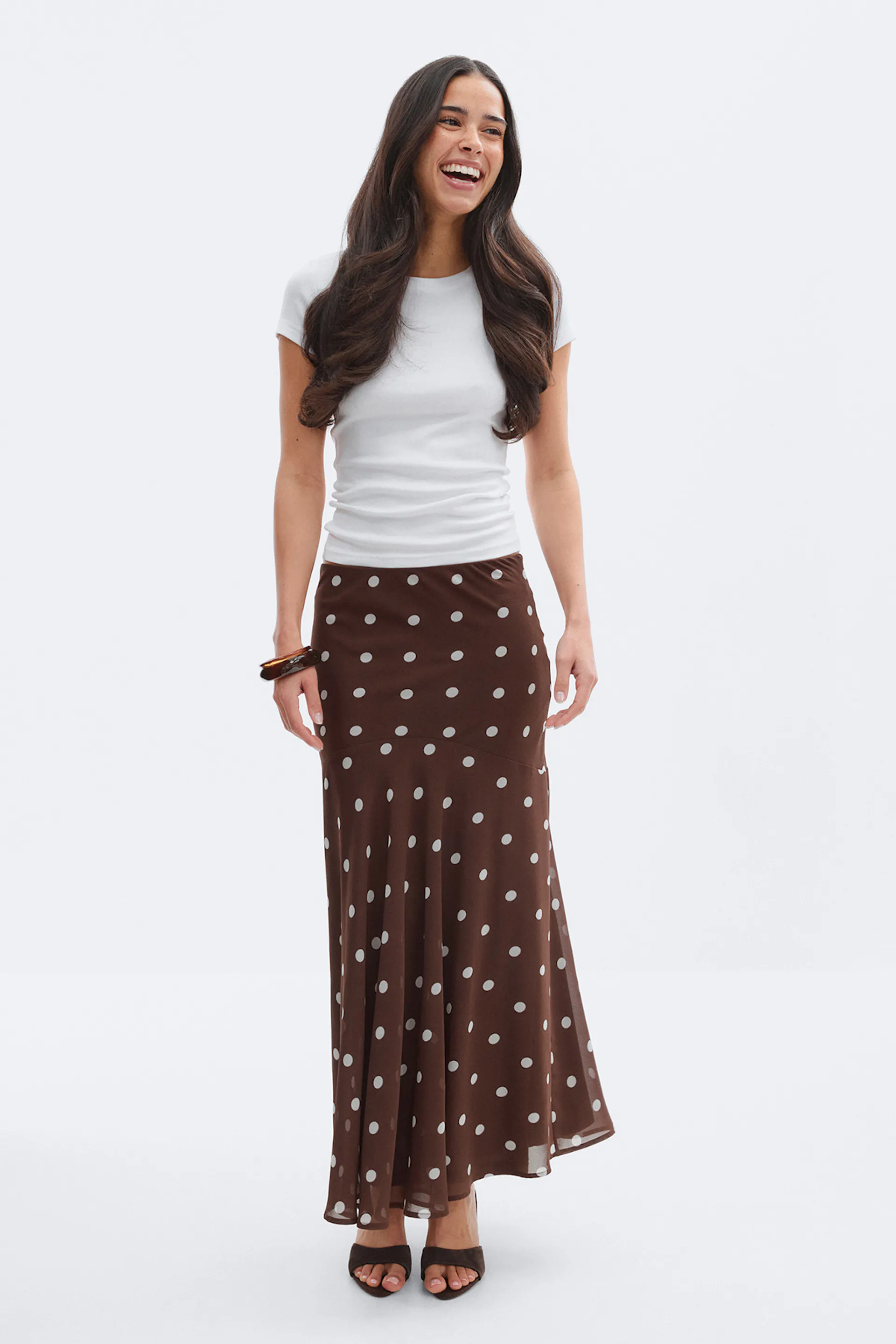 Hvit, kortermet T-skjorte med rund hals, brunt maxiskjørt med hvite prikker, brune, åpne hæler og et armbånd i skilpaddeskall.