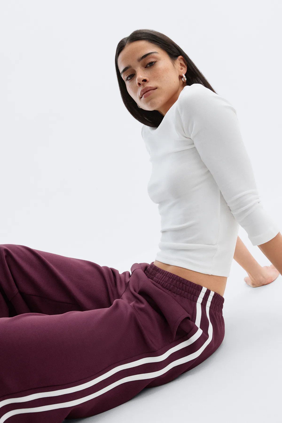 Figursyet hvid top med trekvartærmer sammen med bordeauxfarvede træningsbukser med elastisk linning og to hvide sidestriber.