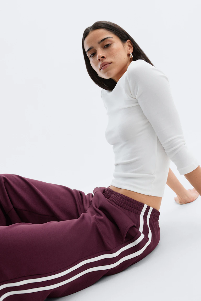 Witte top met driekwart mouwen in combinatie met een bordeauxrode trainingsbroek met elastische tailleband en dubbele witte zijstrepen.