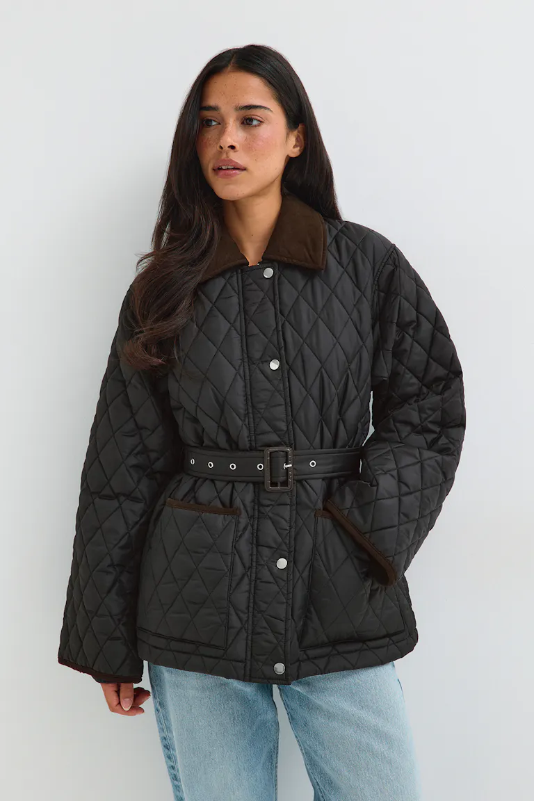 Gesteppte schwarze Jacke mit Gürtel und braunem Kragen, kombiniert mit hellblauen Jeans.