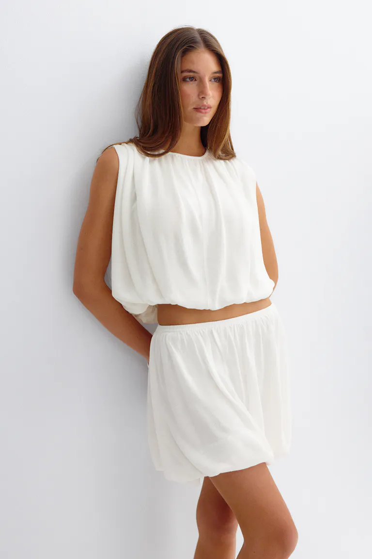 Mouwloze witte gerimpelde blouse met een blousonzoom, gecombineerd met een bijpassende loose-fit short met elastische taille.