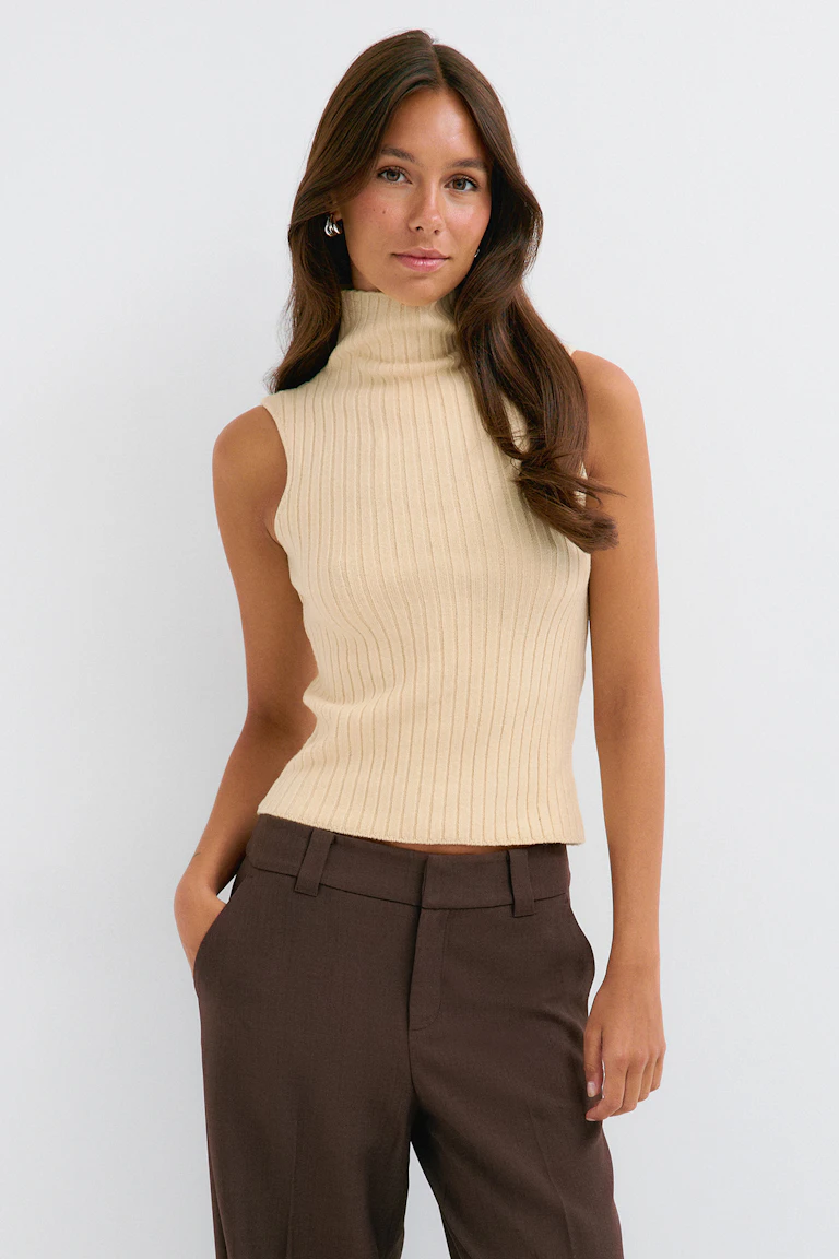 Cream ribbed sleeveless turtleneck top with dark brown tailored trousers.