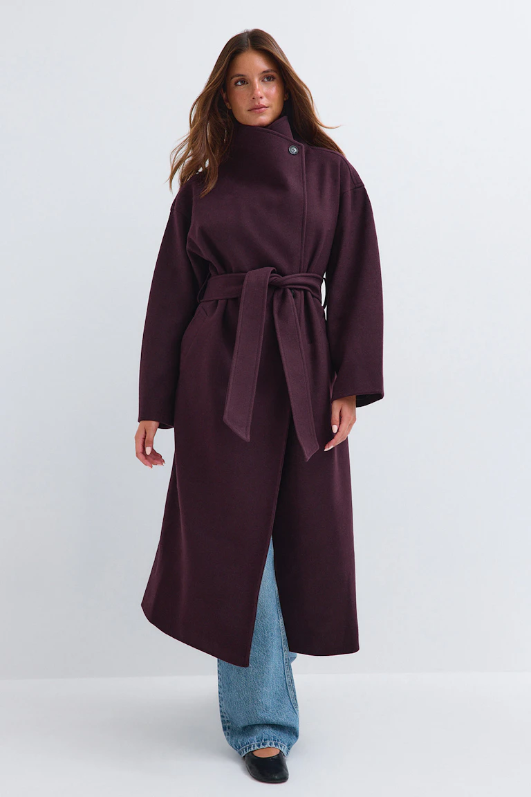 Ein dunkelpflaumfarbener Mantel mit Gürtel, hellblaue Jeans mit geradem Bein und schwarze Ballerinas.