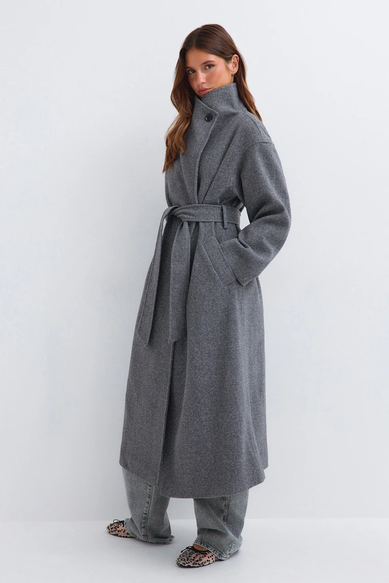 Grey belted coat with a high collar, wide-leg jeans, and leopard-print flats.