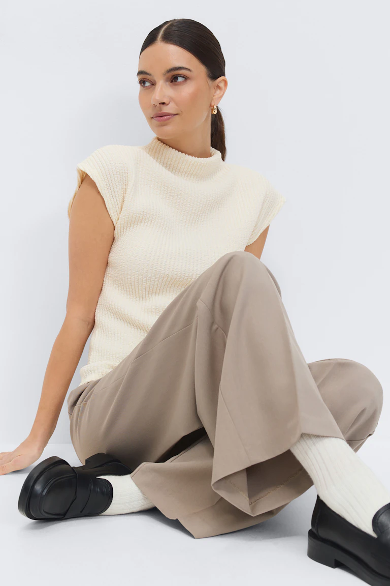 Cream ribbed sleeveless mock‑neck top, beige wide‑leg trousers, white ribbed socks, black leather loafers, and small gold hoop earrings.