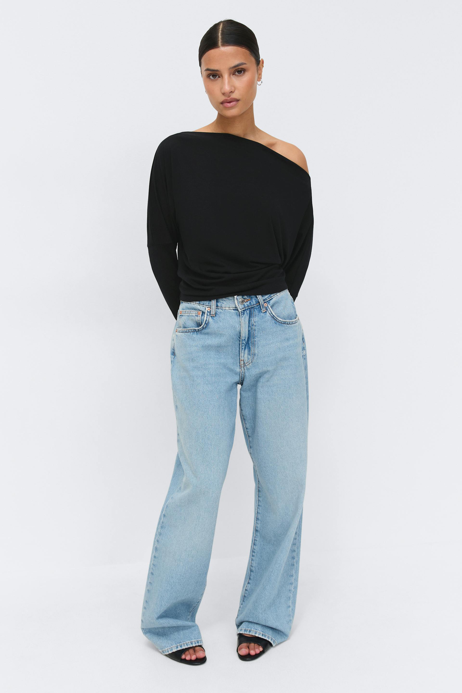 Svart langermet topp uten skuldre med lange ermer kombinert med lyse jeans med høy midje og vide ben og svarte sandaler med åpne hæler.