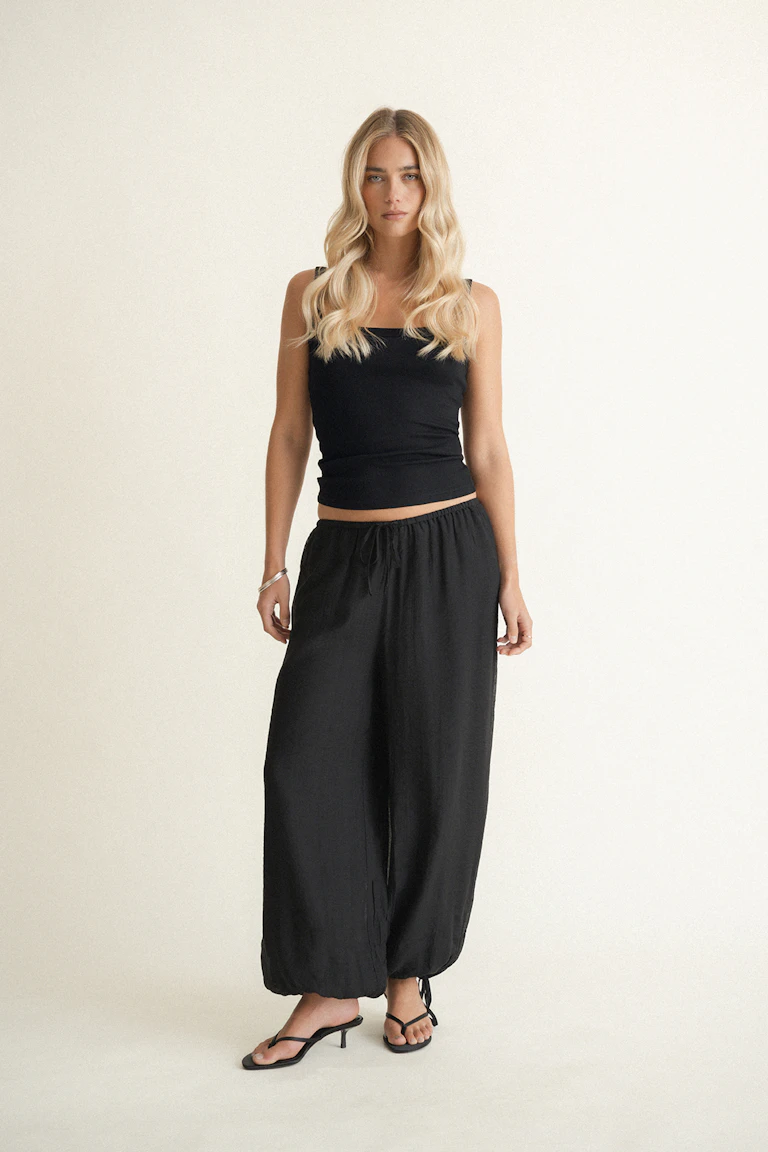 Black ribbed, fitted square-neck tank with wide straps layered over a white halter-neck top; paired with black drawstring sweatpants.