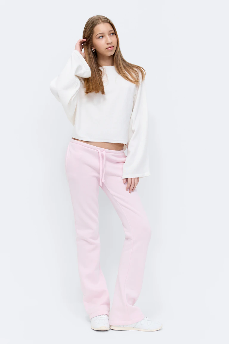 Blassrosa kurzärmeliges, tailliertes Oberteil, passende blassrosa Jogginghose mit Kordelzug und beige-weiße Schnürsneakers.