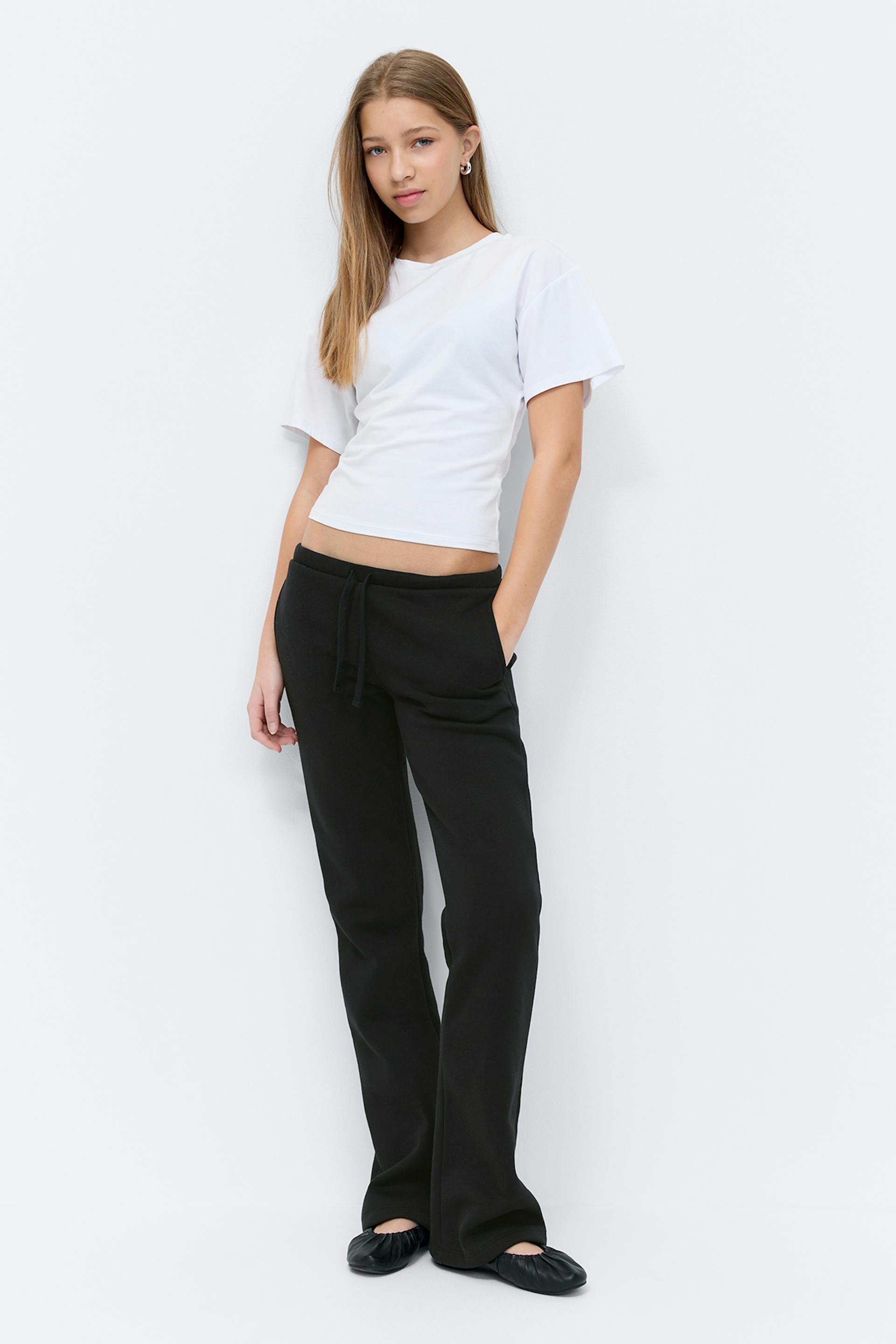 White short-sleeve crewneck T‑shirt, black wide-leg trousers, and black low-top sneakers with white stripes and gum soles.