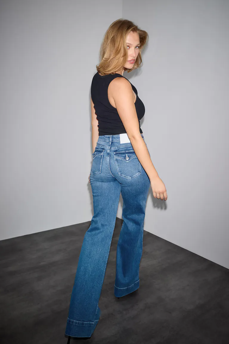 Sort ærmeløs tanktop sat sammen med højtsiddende mellemblå flared jeans med manchetter og baglommer med knapper.