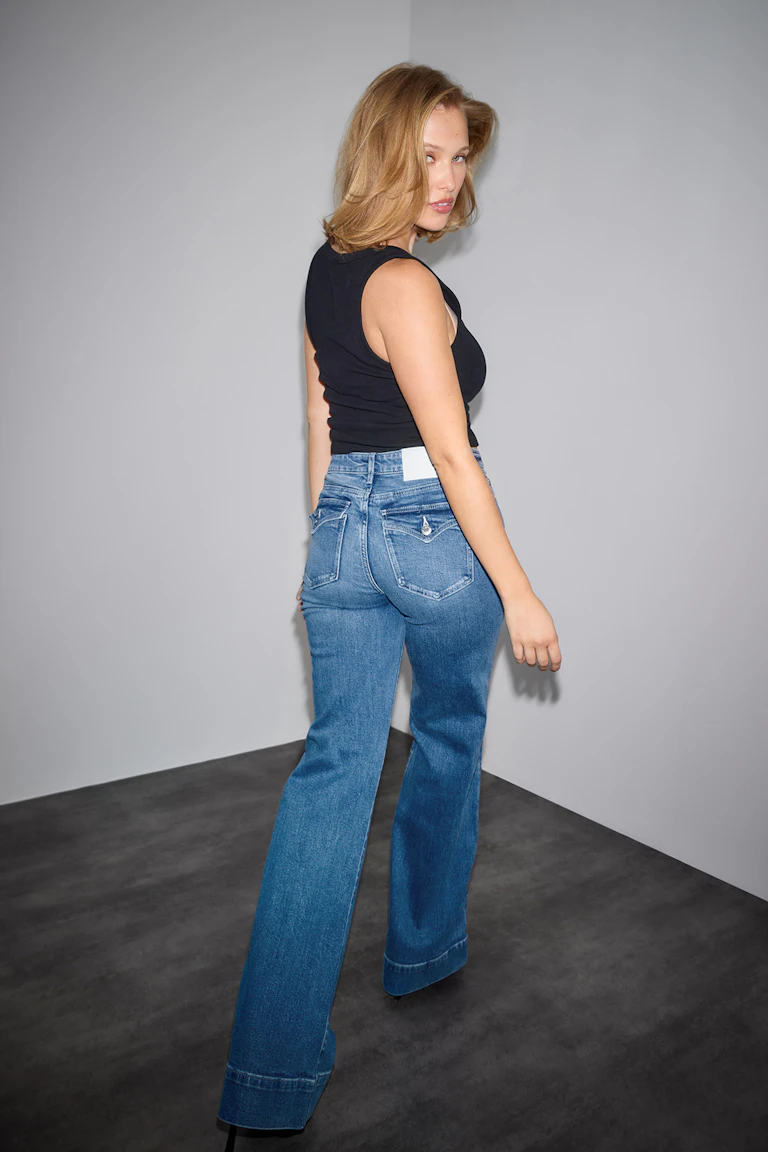 Black sleeveless tank top paired with high‑rise medium-blue flared jeans featuring cuffed hems and buttoned back pockets.