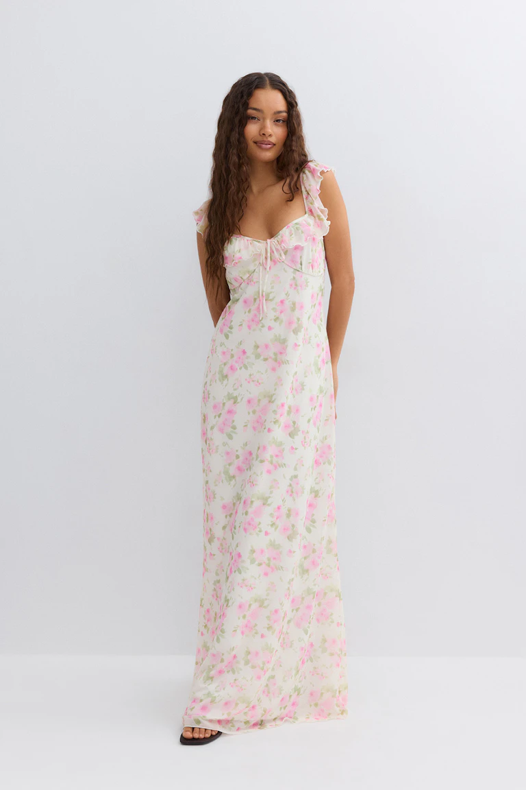 Ruffle-trimmed floral-print maxi slip dress in soft pink and green on white with a sweetheart neckline and front tie, paired with black open-toe sandals.