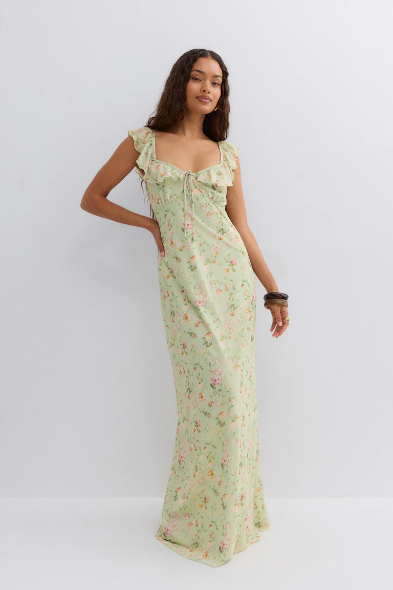 Floor-length pale green floral slip dress with ruffled cap sleeves and a sweetheart tie-front neckline, styled with stacked bangle bracelets.