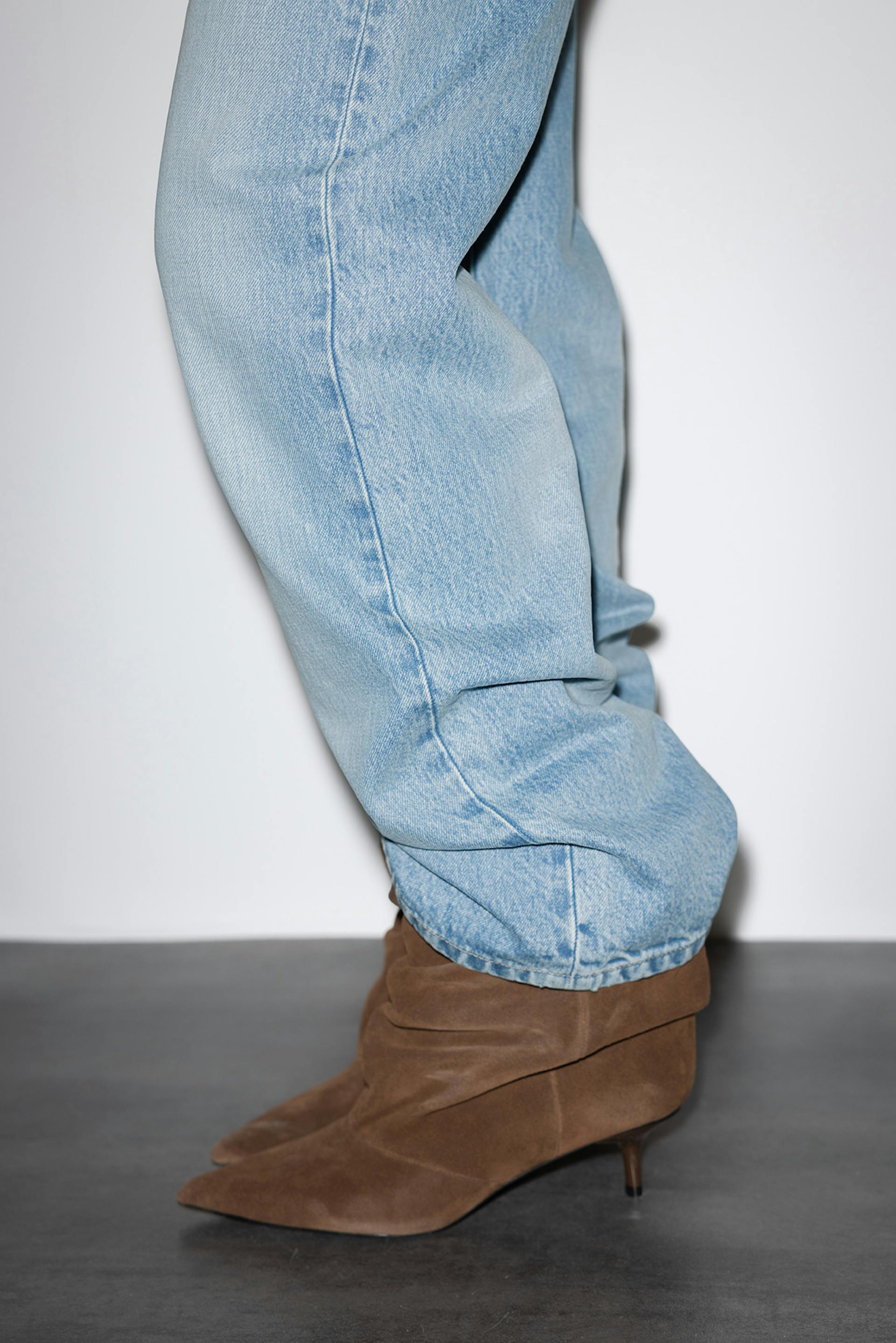 Light-wash relaxed-fit denim jeans worn over brown suede pointed-toe ankle boots with low kitten heels.