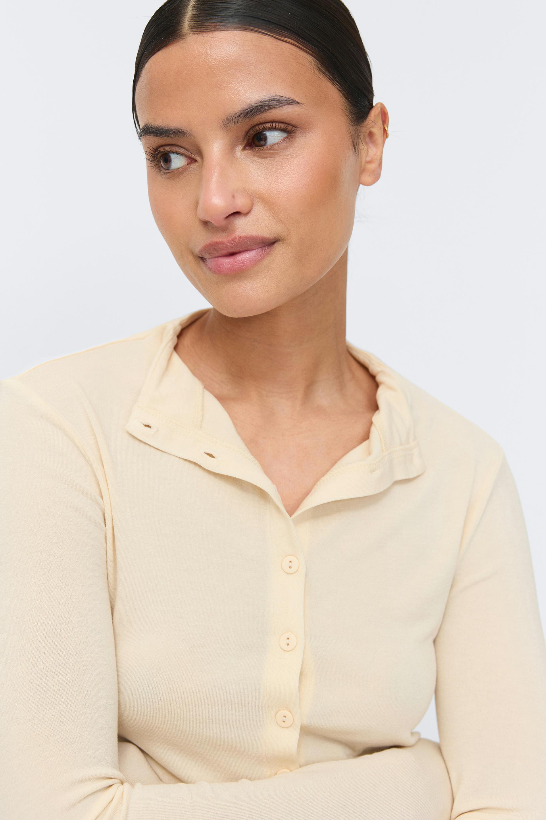 Pale cream long-sleeve button-up knit top with a relaxed collar and round buttons.