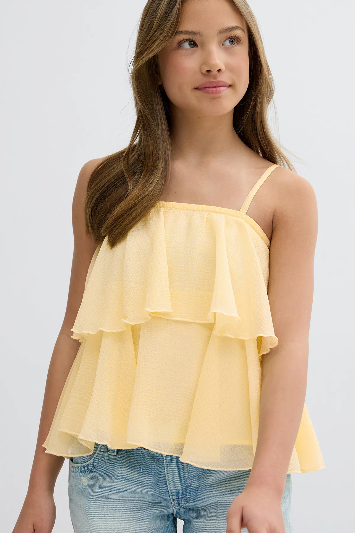 Light yellow tiered ruffle camisole with thin spaghetti straps, paired with light-wash denim jeans.