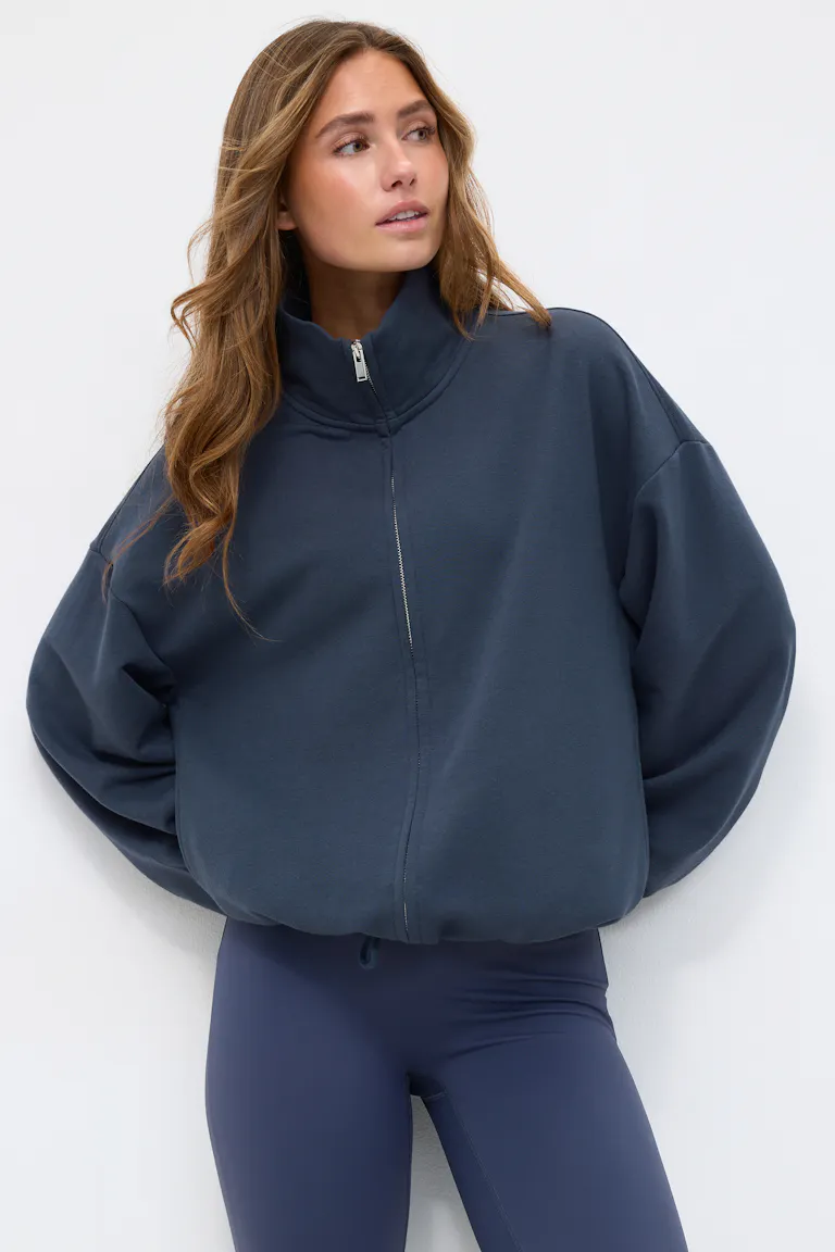 Dunkelmarinefarbenes Oversize-Sweatshirt mit Reißverschluss, hohem Trichterkragen, Ballonärmeln und Kordelzug am Saum, kombiniert mit marinefarbenen Leggings mit hoher Taille.