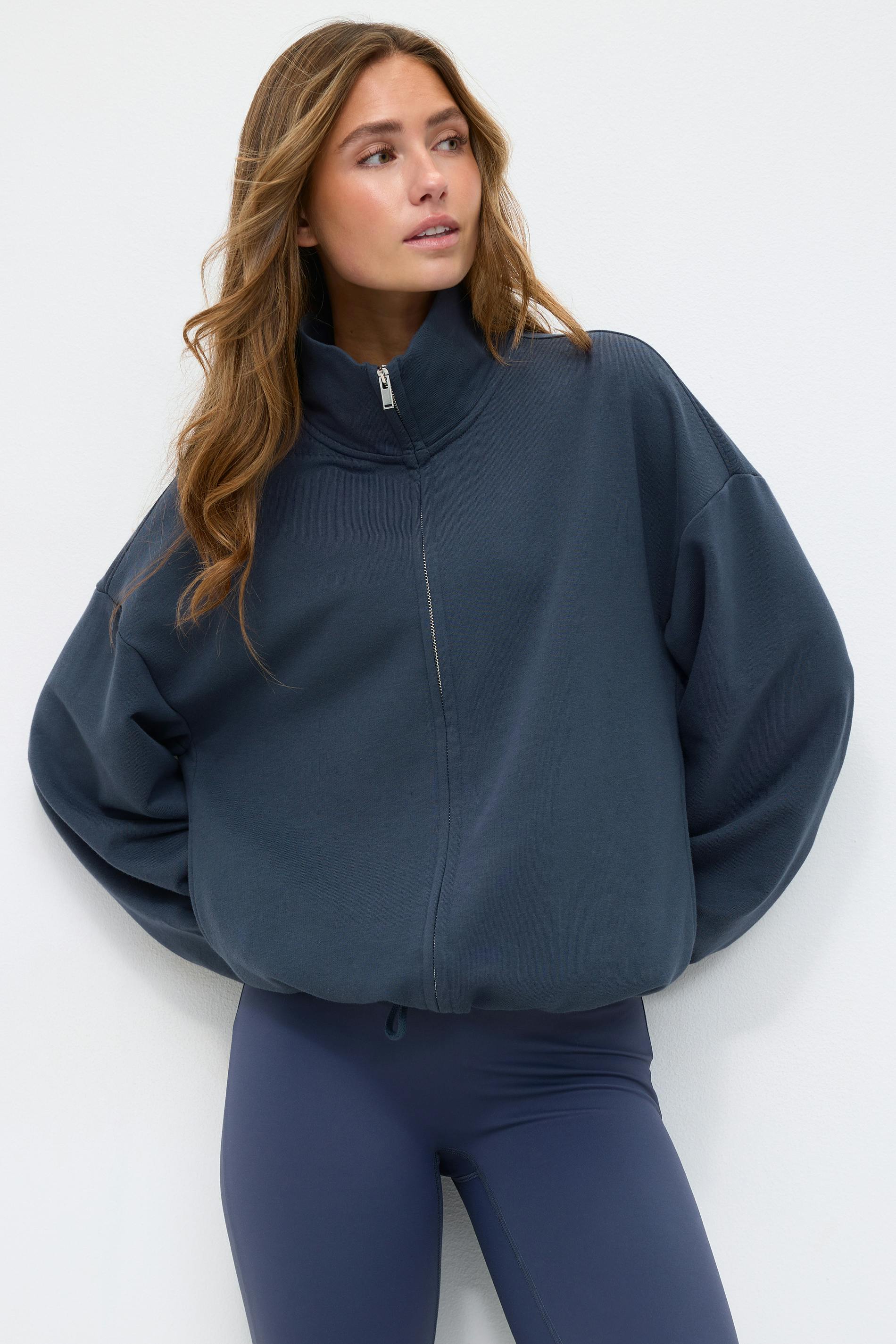 Dark navy oversized zip-front sweatshirt with a high funnel collar, balloon sleeves and drawstring hem, paired with high-waist navy leggings.