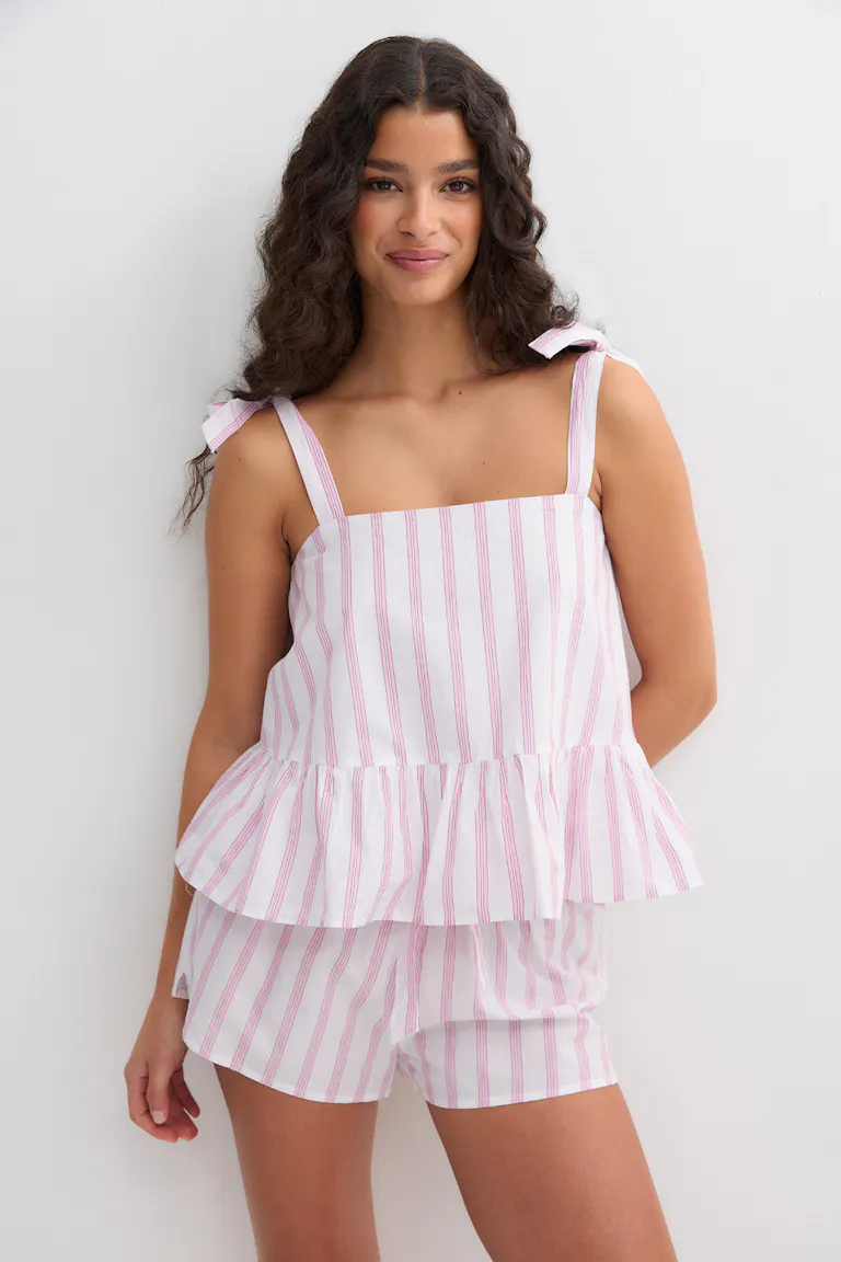 Vit camisole med rosa vertikala ränder, fyrkantig halsringning, knutna axelband och peplum-fåll, kombinerad med matchande randiga shorts.