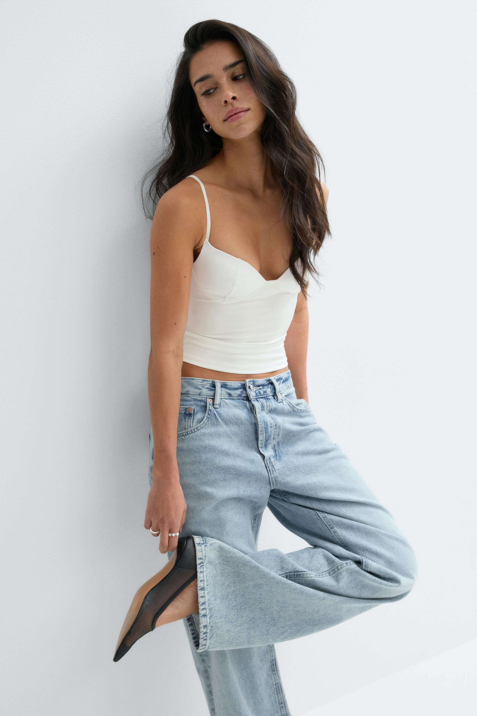 Valkoinen sovitettu, leikattu pusero, jossa on ohuet spagettihihnat ja herttainen pääntie, yhdistettynä vaaleisiin, korkeavyötäröisiin, leveälahkeisiin farkkuihin ja mustiin teräväkärkisiin verkkokorkokenkiin.