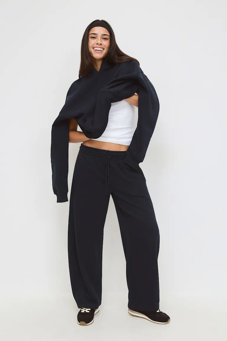 White cropped tank top; black oversized sweatshirt draped over the shoulders; black wide-leg drawstring sweatpants; black sneakers with white laces and tan soles; black headband.
