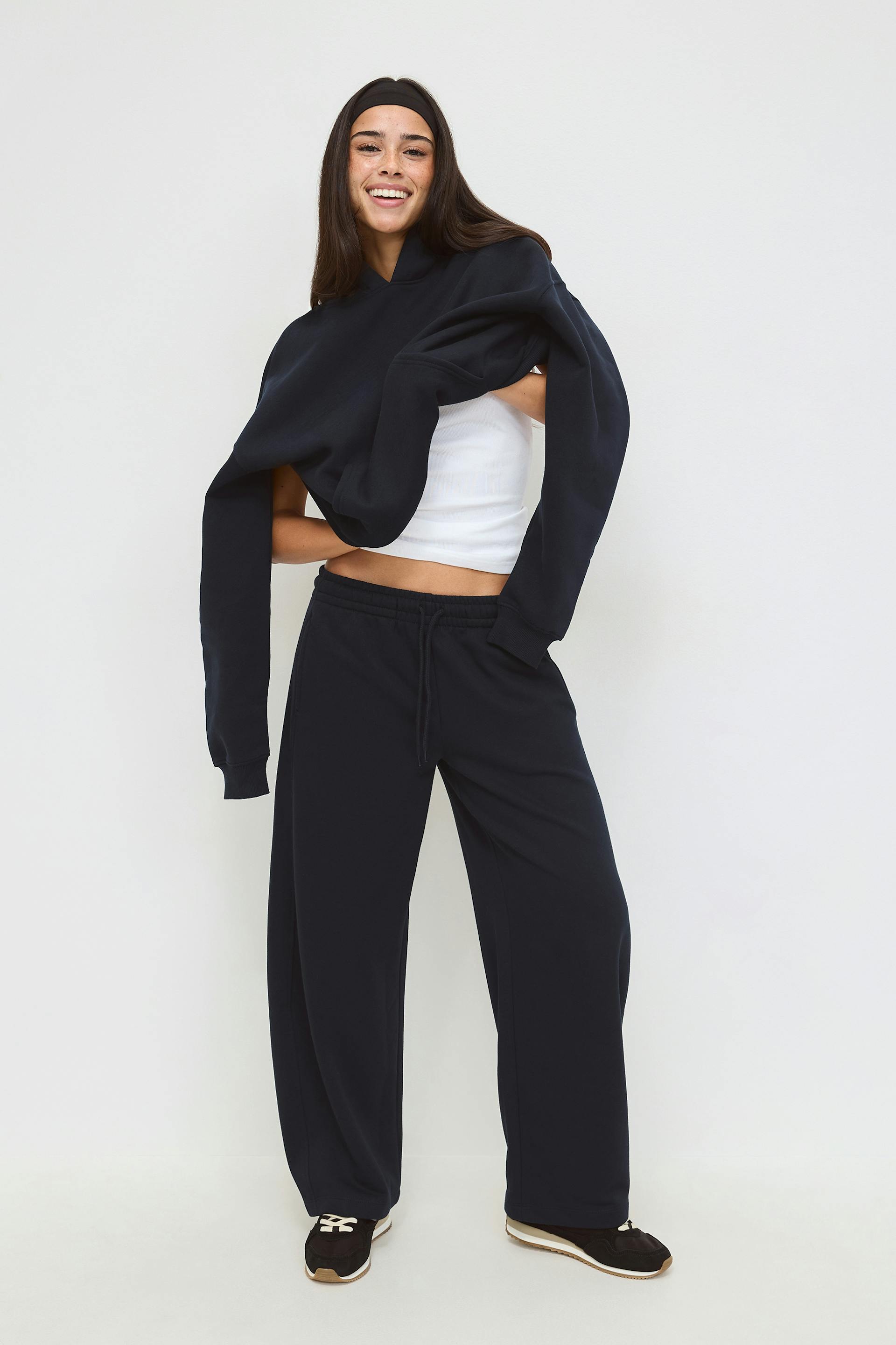 Hvit, kort tanktop, svart oversized genser drapert over skuldrene, svarte sweatpants med vidde ben og snøring, svarte joggesko med hvite lisser og solbrune såler, svart pannebånd.