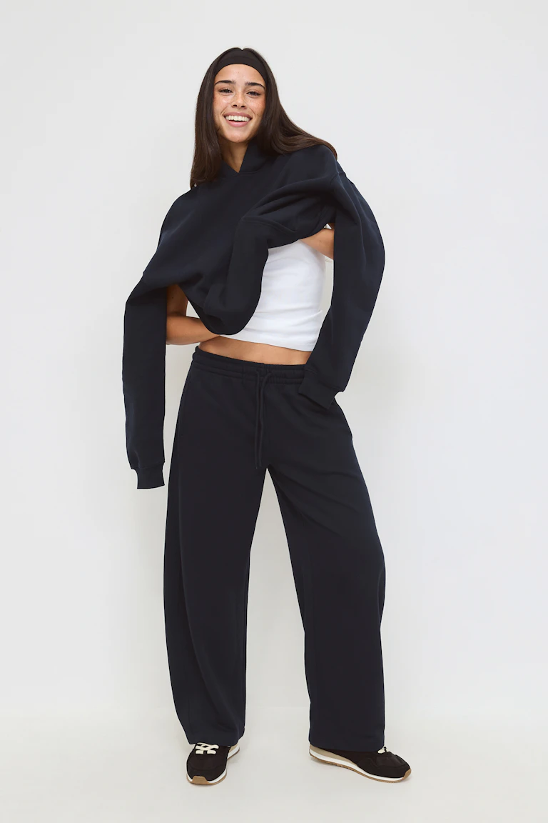 White cropped tank top; black oversized sweatshirt draped over the shoulders; black wide-leg drawstring sweatpants; black sneakers with white laces and tan soles; black headband.