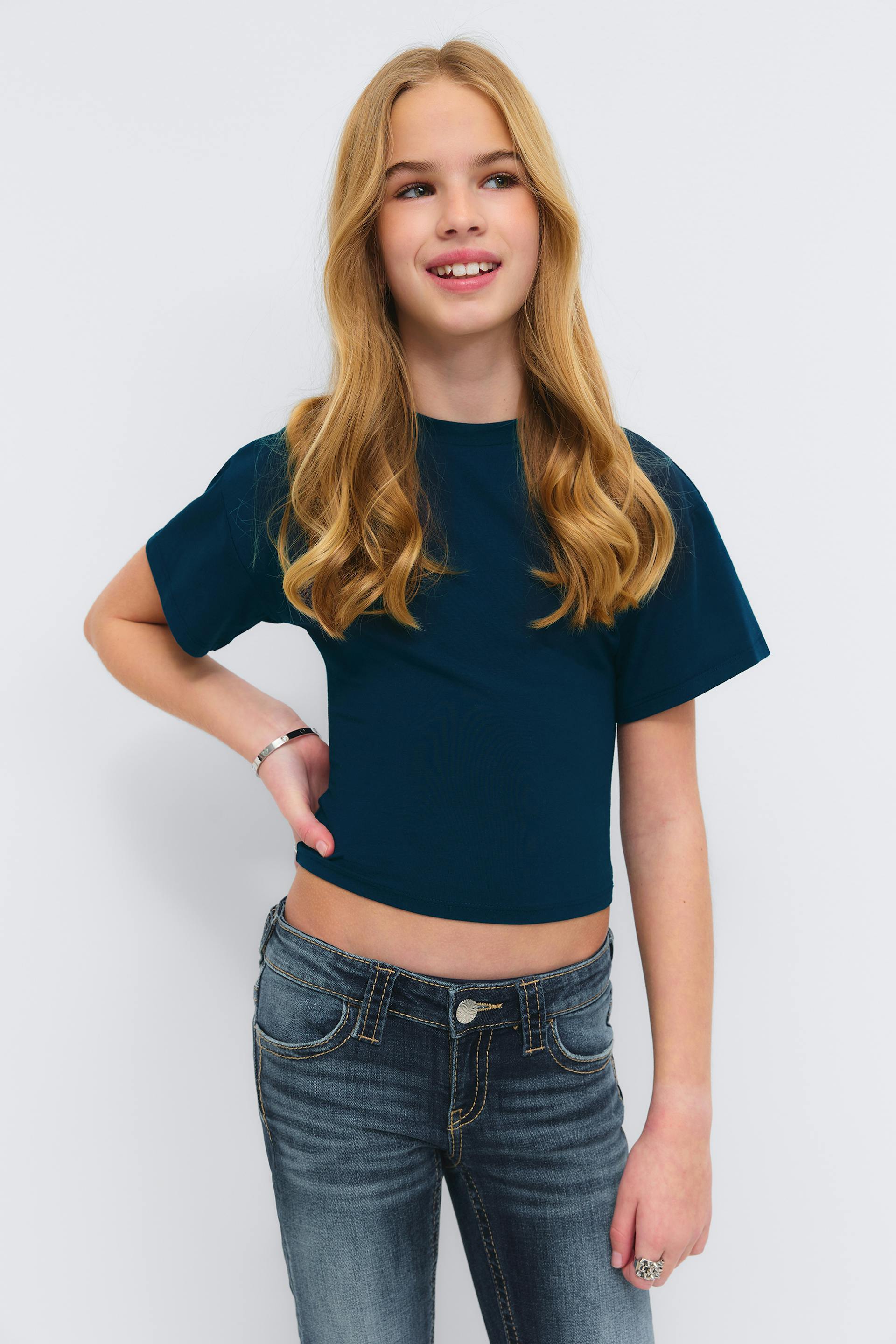 Deep teal short-sleeve cropped T-shirt paired with faded mid-rise skinny jeans, accessorized with a silver bangle and a silver statement ring.