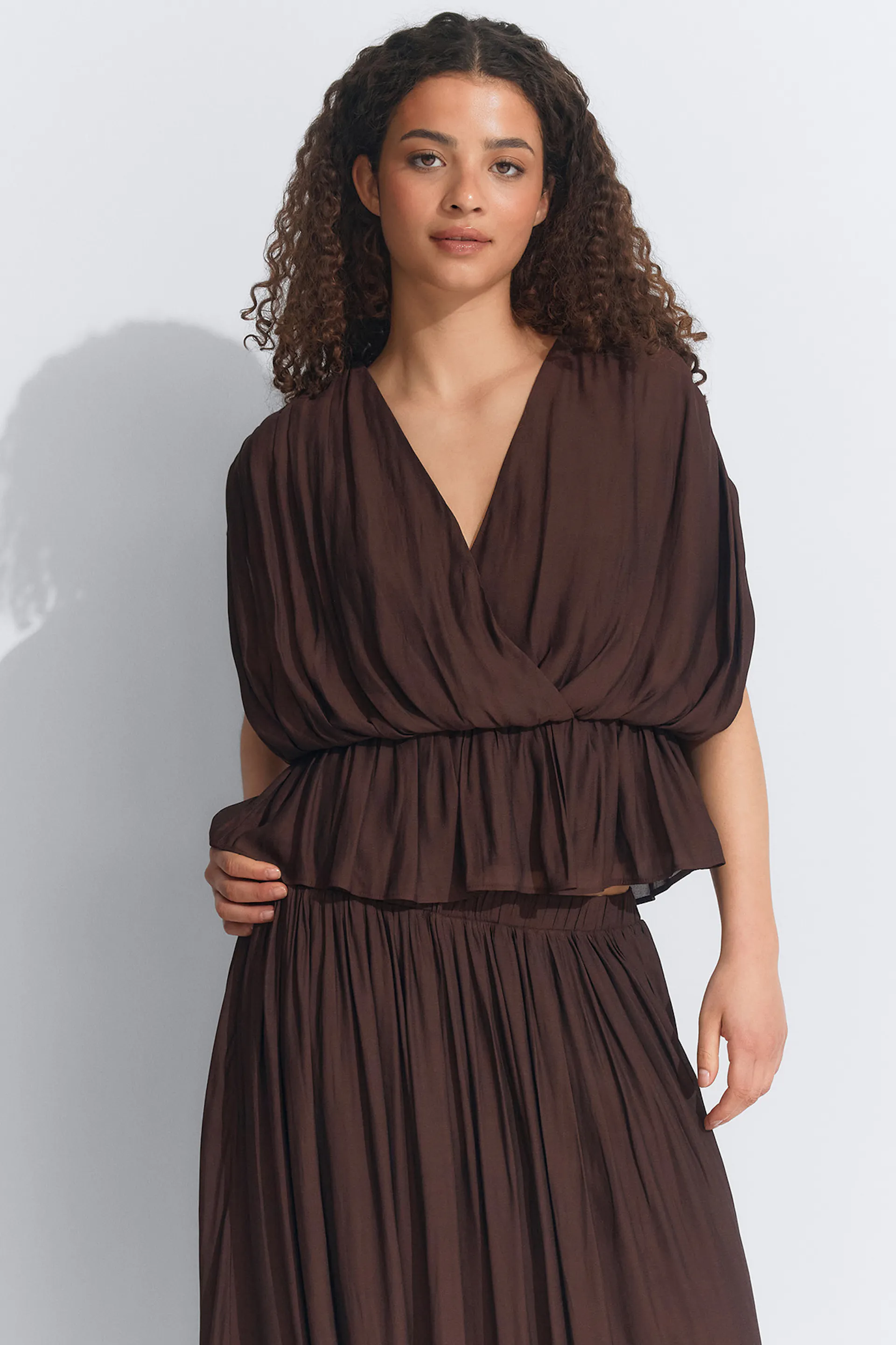 Dunkelbraune, geraffte Schößchenbluse mit V-Ausschnitt und kurzen, drapierten Ärmeln, gepaart mit einem passenden, hochtaillierten Falten-Maxirock.