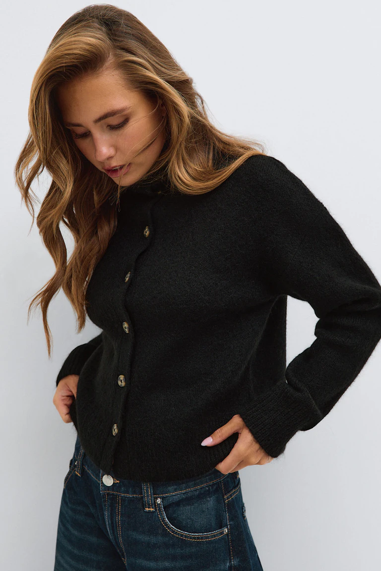 Schwarze Strickjacke mit Knopfleiste und dunkelblaue Jeans.