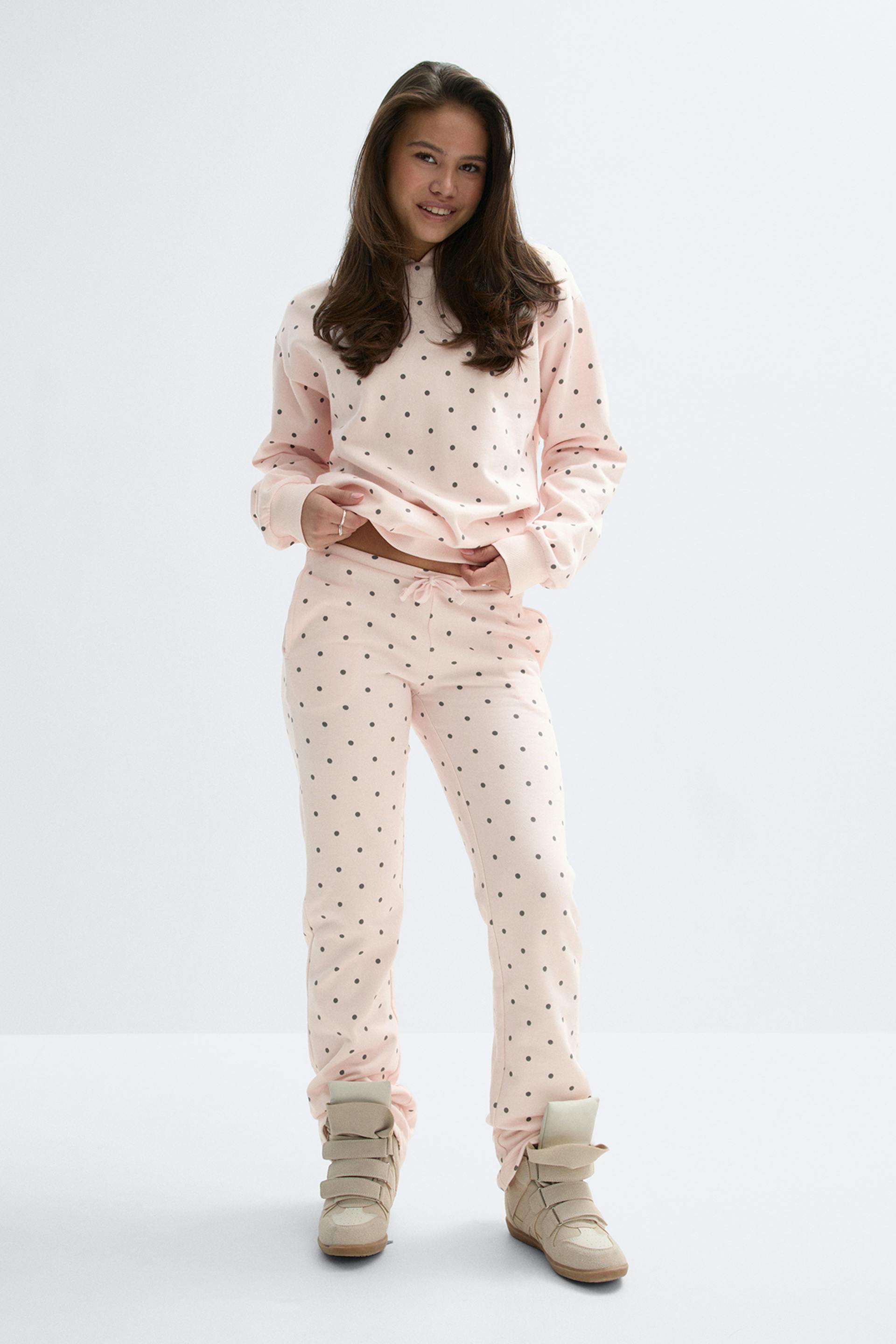 Ensemble loungewear rose clair à petits pois noirs - sweat à manches longues et pantalon de jogging à cordon - associé à des baskets montantes beiges à fermetures à lanières.