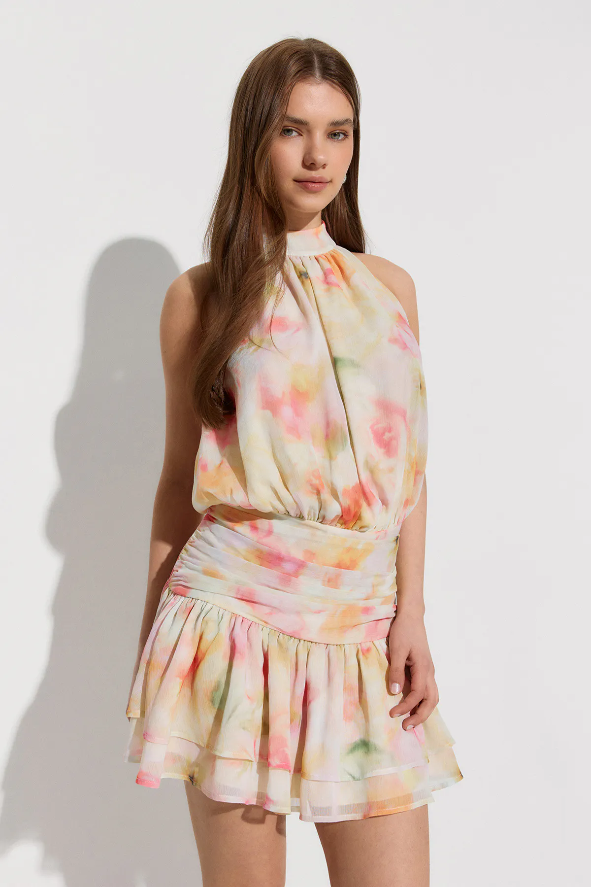 Sleeveless halter-neck dress in a pastel watercolor floral print, with a gathered blouson bodice, wide ruched waistband and tiered ruffle mini skirt.
