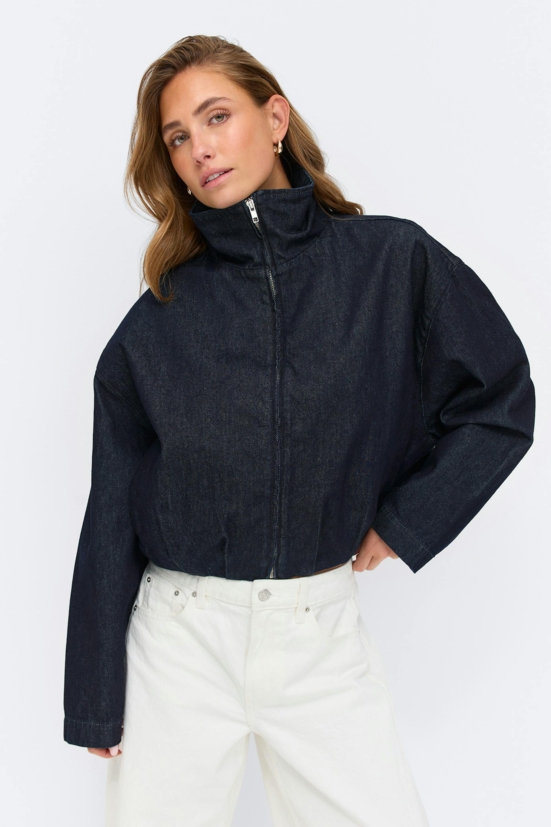 Tumma indigonvärinen, leikattu farkkutakki, jossa on korkea suppilokaulus ja pitkät hihat, yhdistettynä korkeavyötäröisiin valkoisiin suoralahkeisiin farkkuihin.